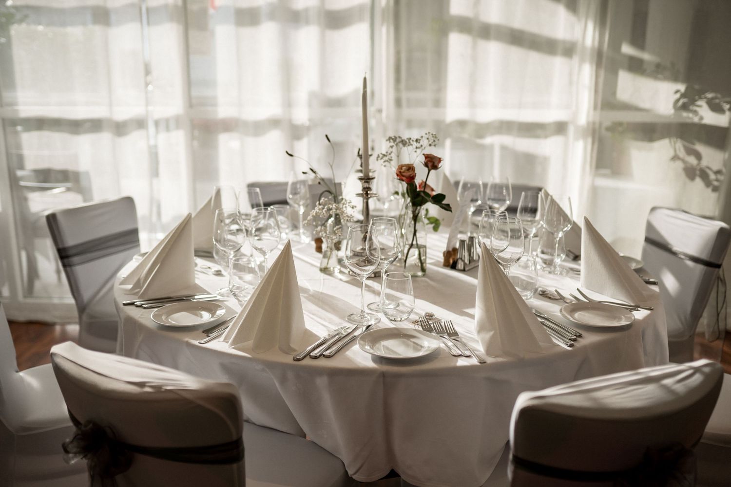Panoramic view of formal dining tables set with white linens and place settings.