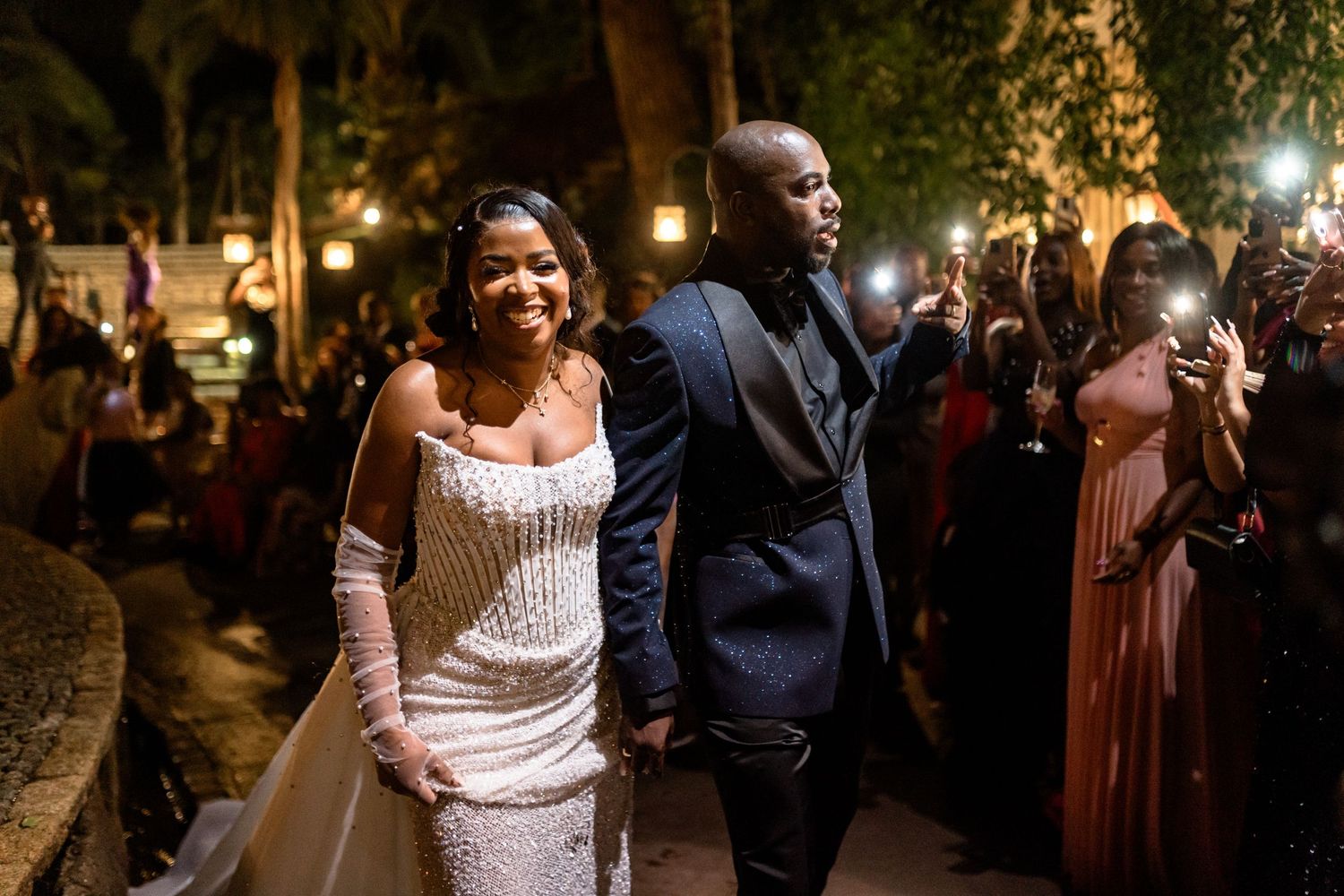 Nighttime celebration with guests gathering along a palm-lined pathway.