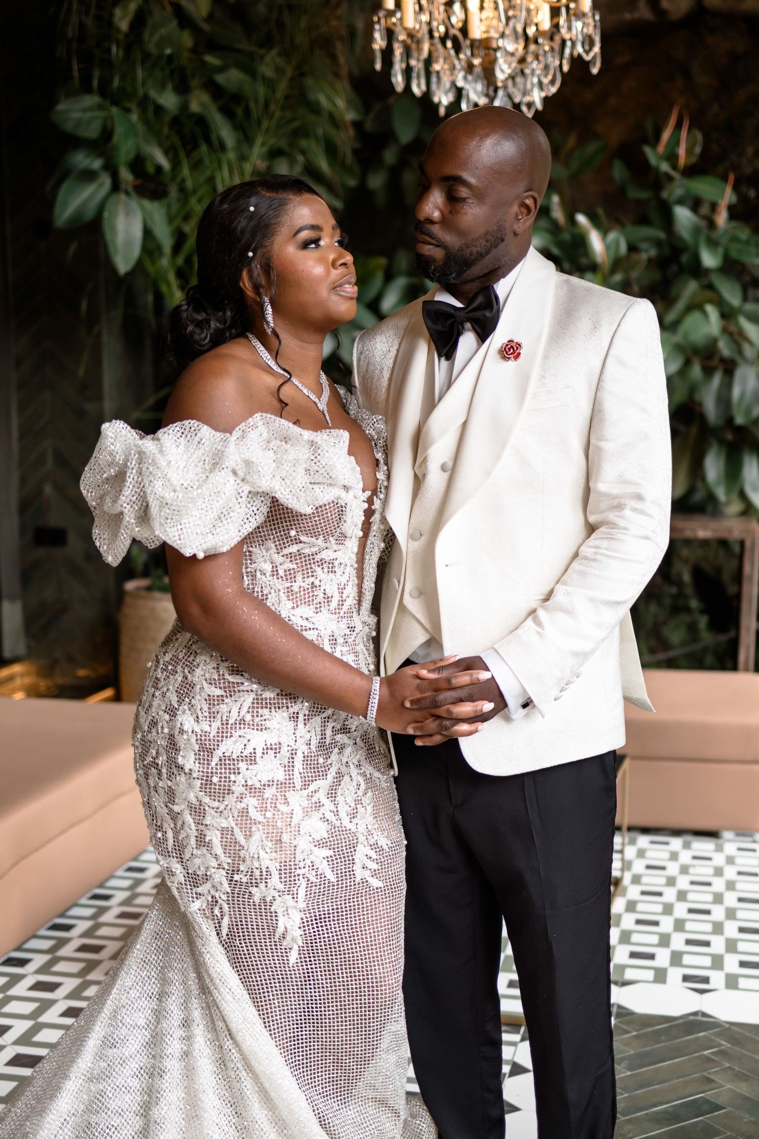 A couple shares an intimate moment in formal attire under a crystal chandelier.