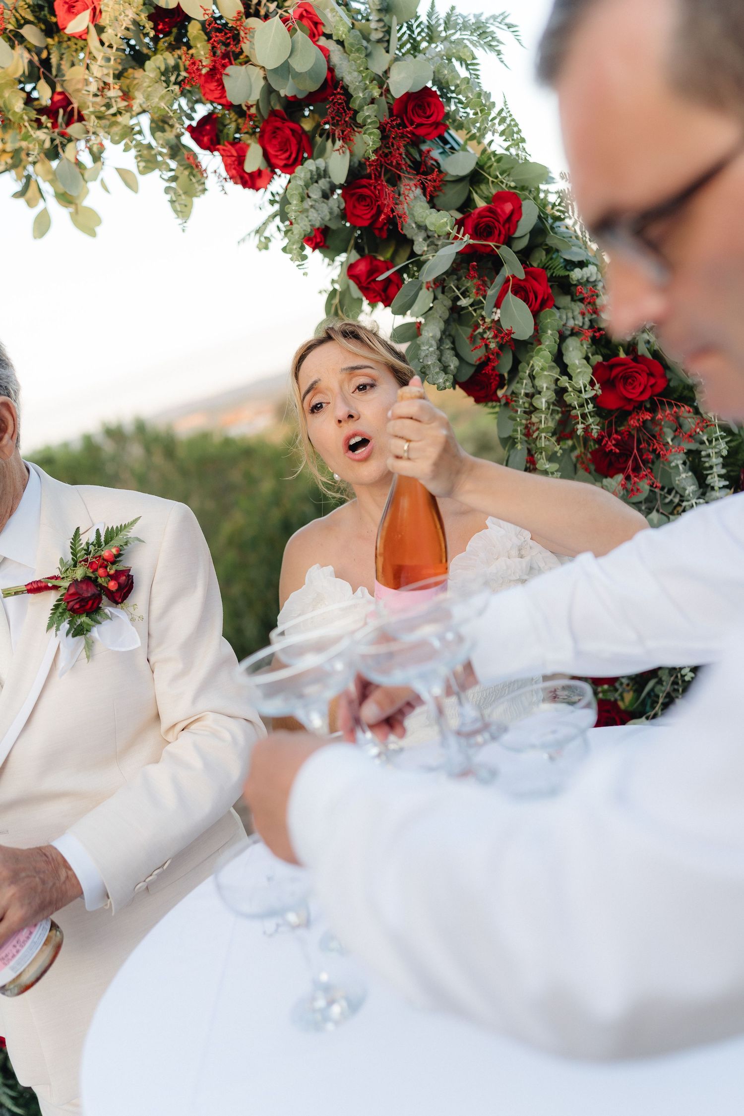 Champagne tower being filled during outdoor wedding reception under floral arch.