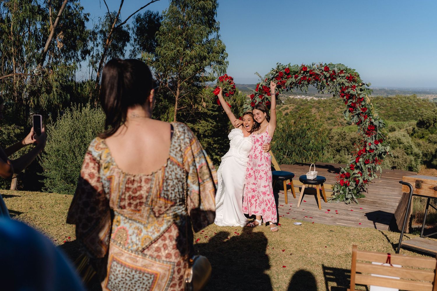 Outdoor wedding venue setup with wooden arch and natural landscape backdrop.