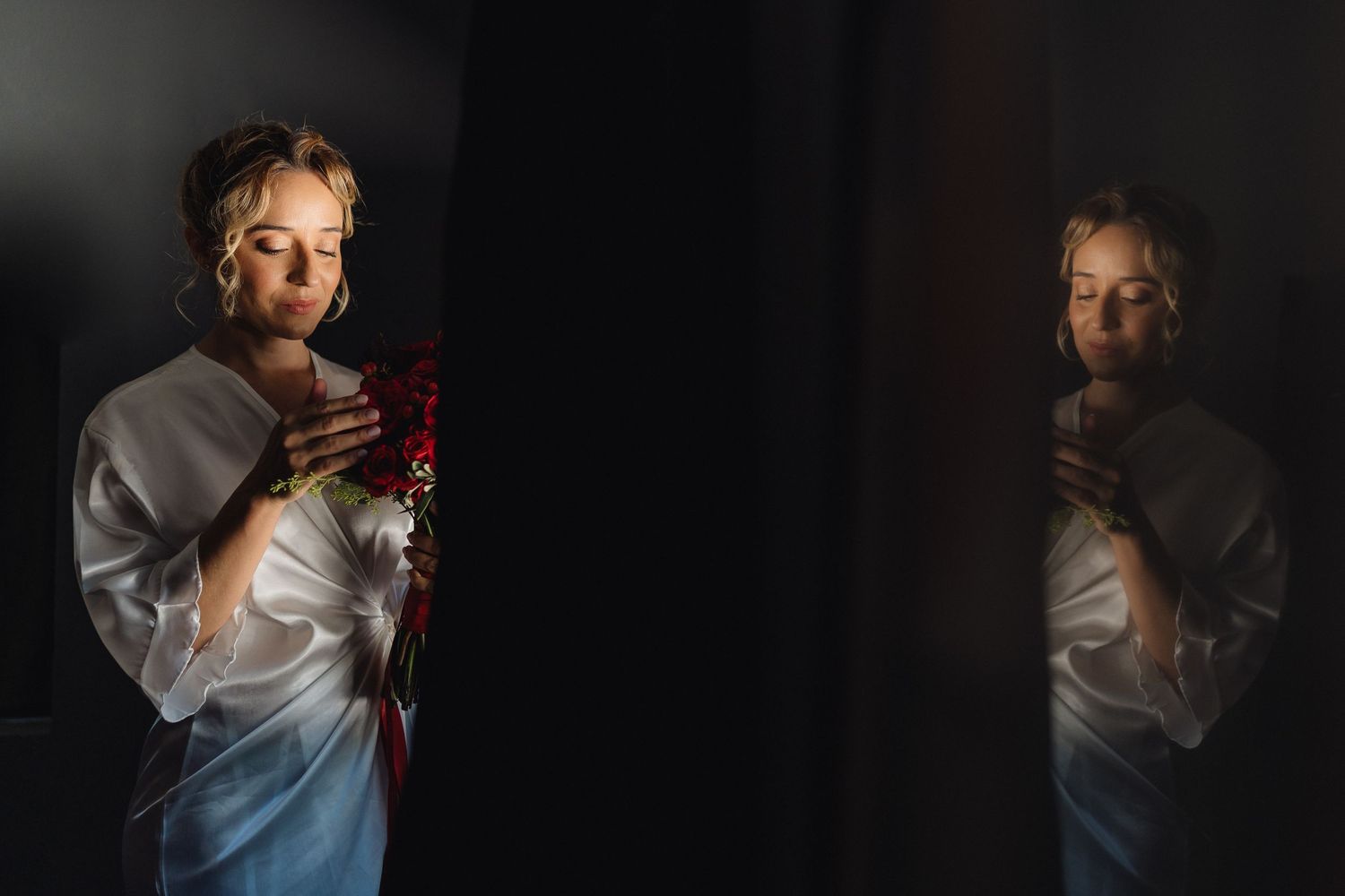 Dramatic low-light portrait with red rose bouquet against dark background.