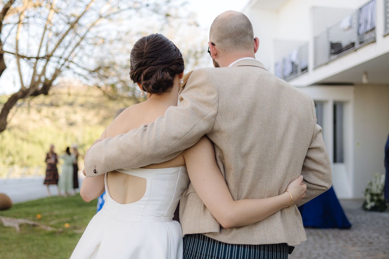 Couple embracing in formal attire against white building exterior.
