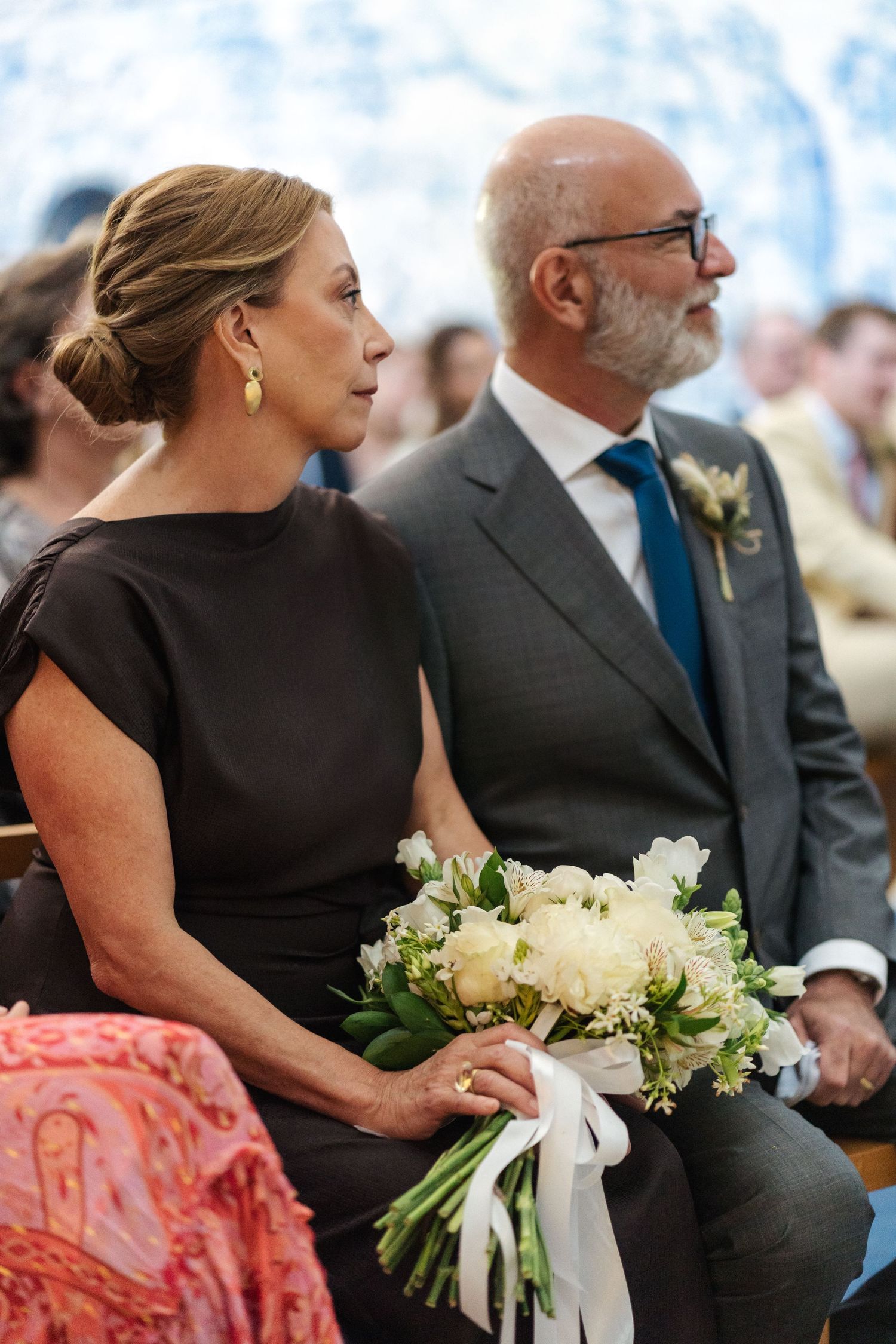 Guests in formal attire seated with white floral bouquets at a wedding ceremony.