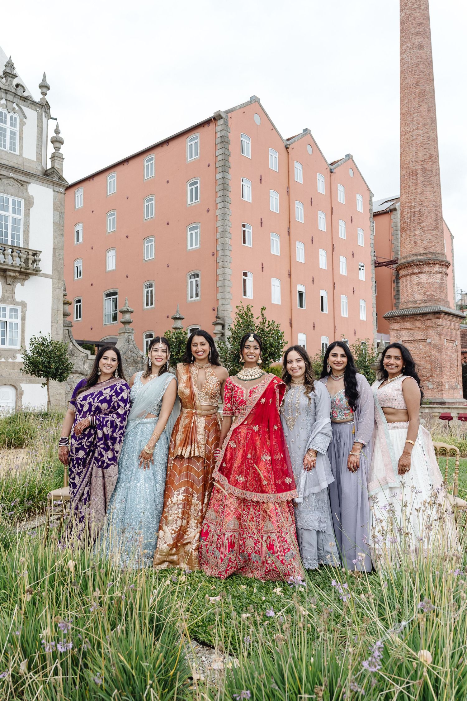 Wedding party in mix of traditional Indian and modern attire poses in front of historic building.