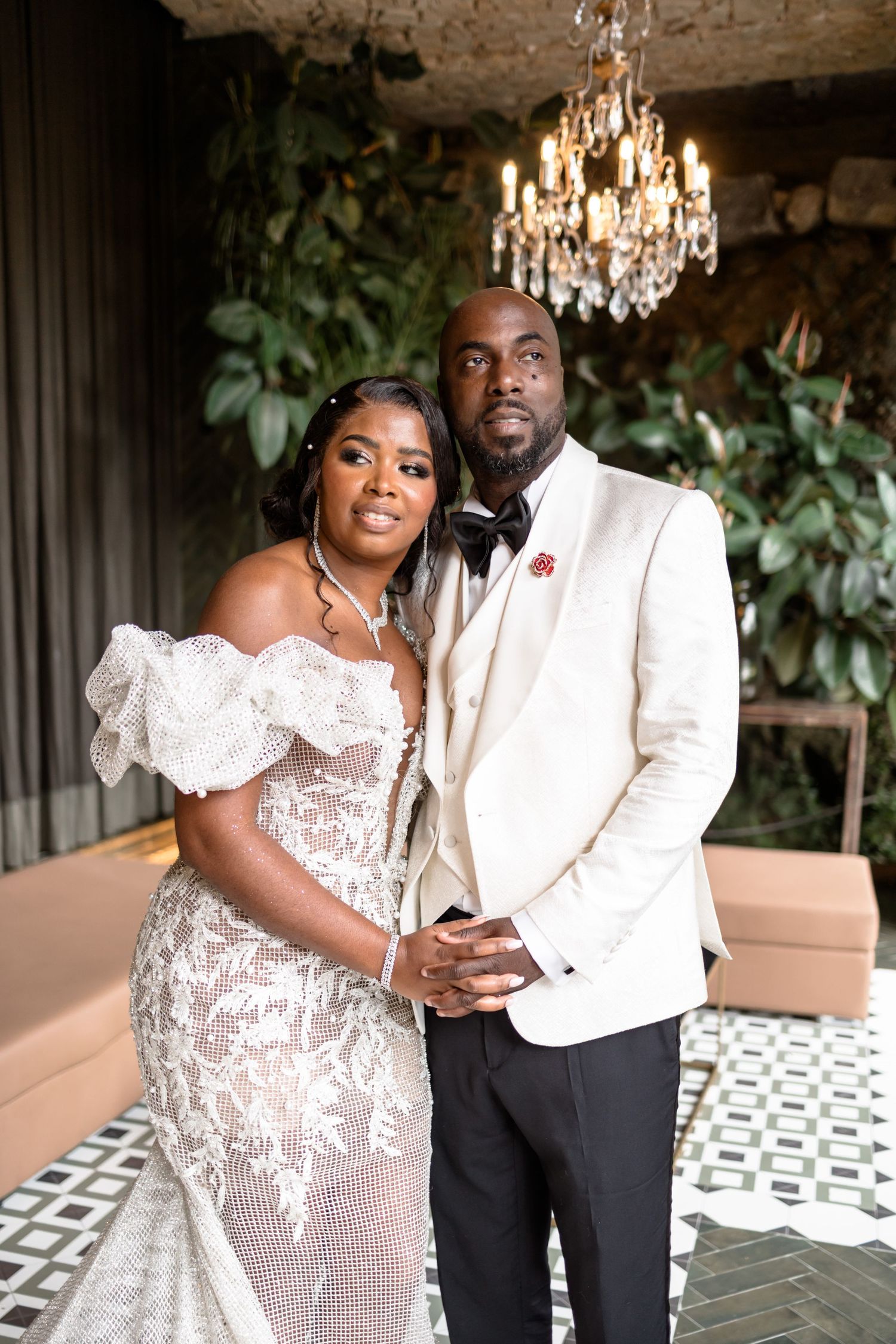 Elegant wedding couple posing beneath a crystal chandelier in a luxurious venue setting.