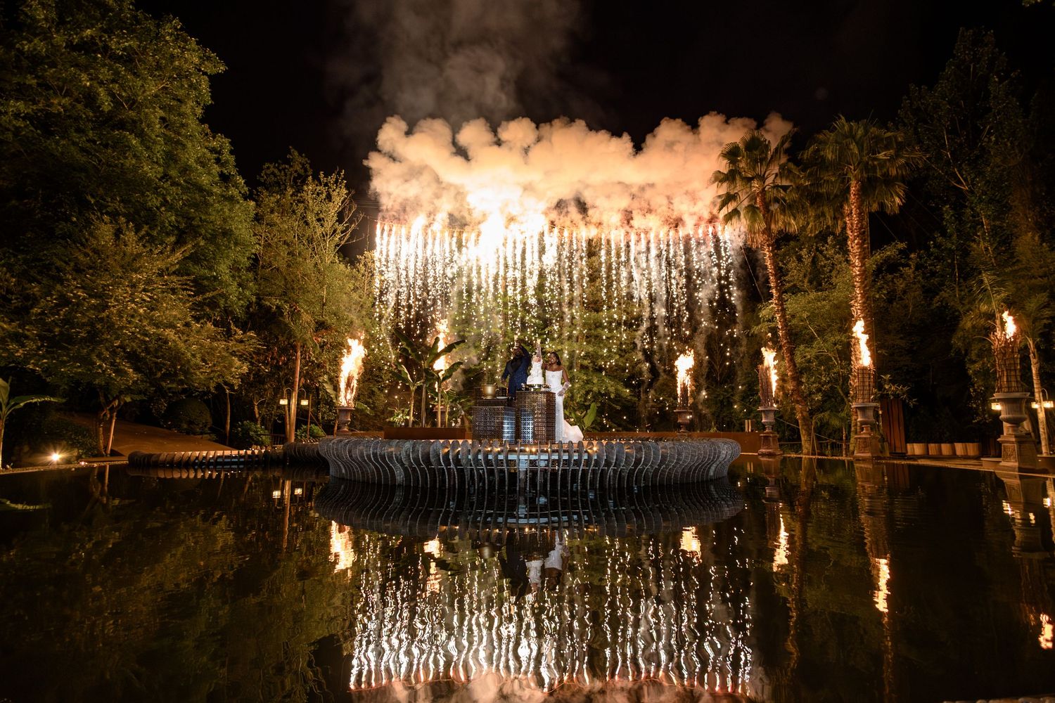 Spectacular fireworks display reflected in a pond during a nighttime wedding celebration.