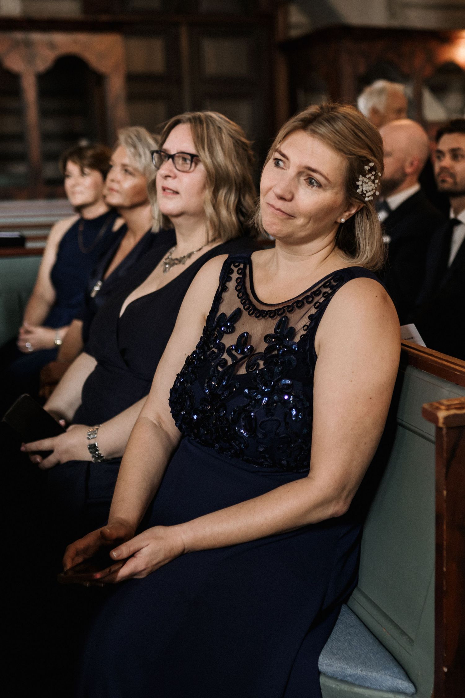 Wedding guests in formal attire seated in church pews during ceremony.