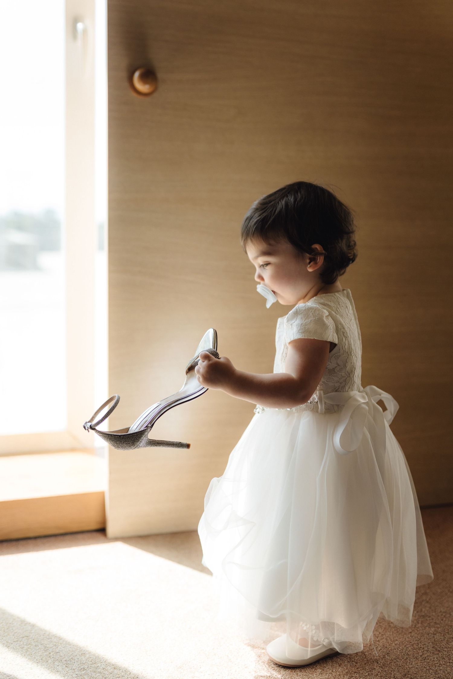 Artistic series of a young flower girl in white dress playing in natural window light.
