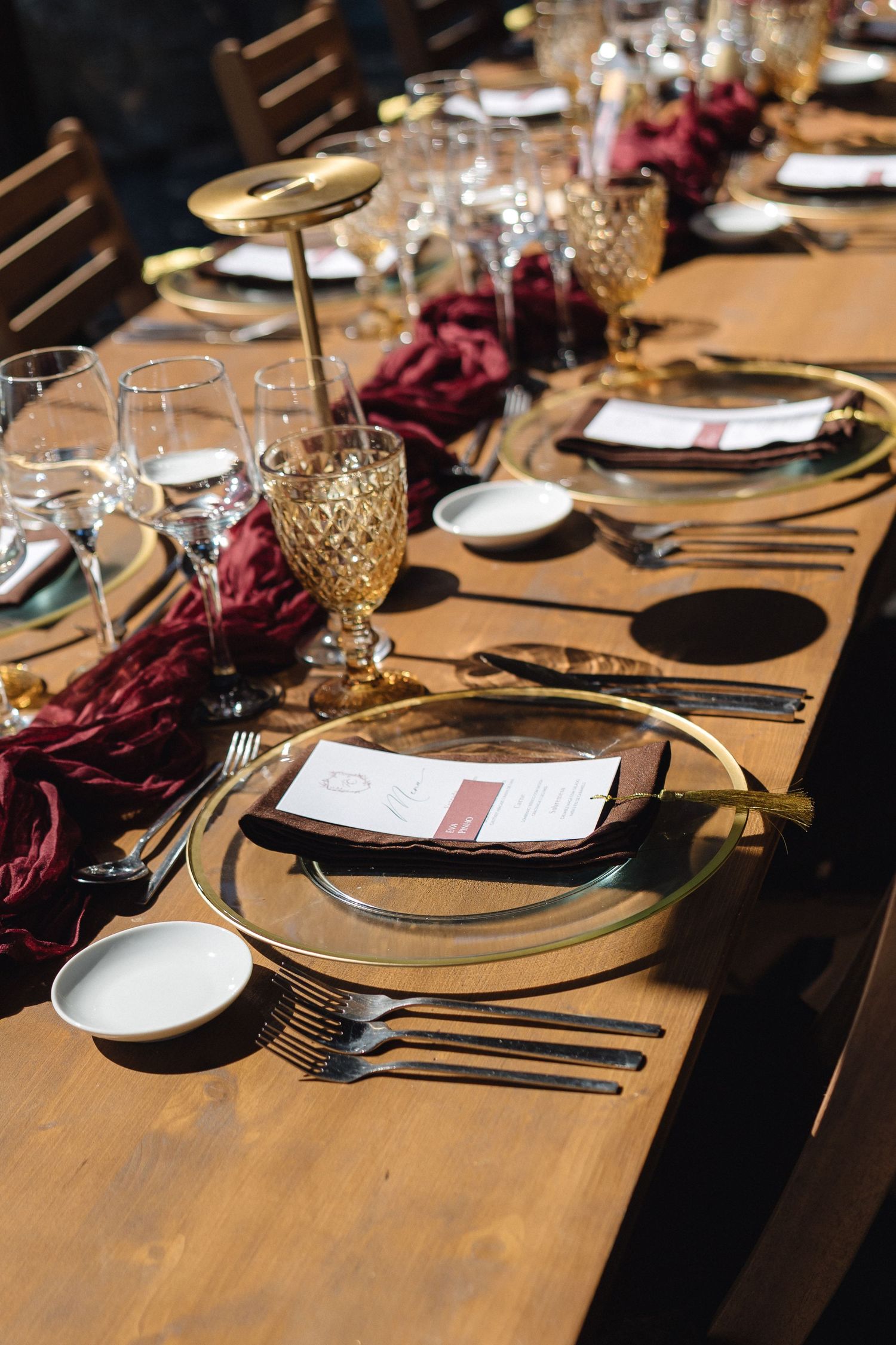 Elegant table setting with gold chargers, burgundy napkins and crystal glassware at a formal event.