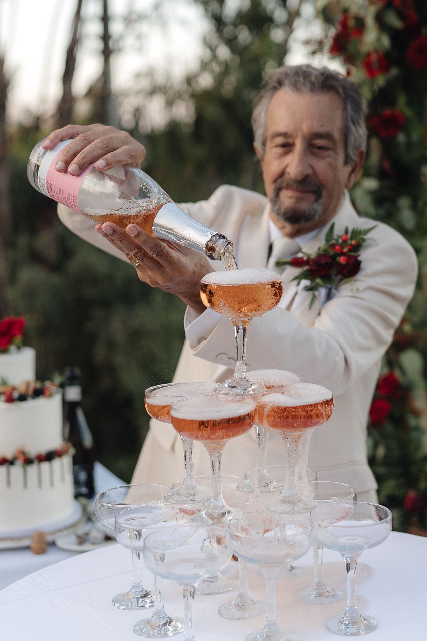 Champagne being poured into a tower of coupe glasses at an elegant wedding reception.