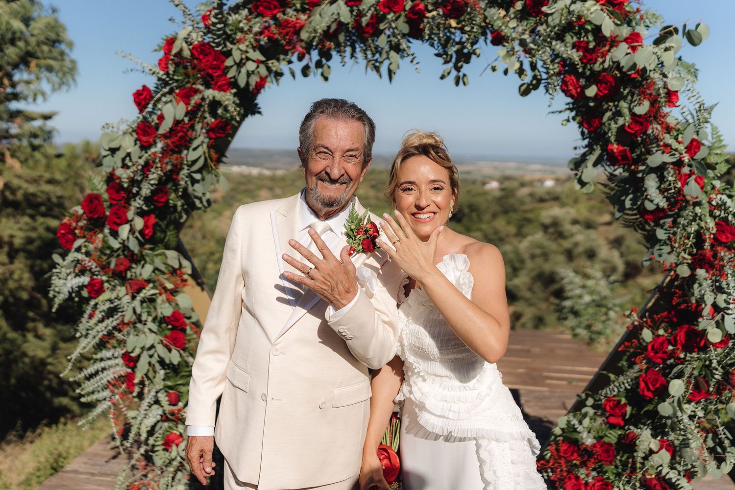 Newlyweds share joyful moments under a dramatic floral arch with red roses.