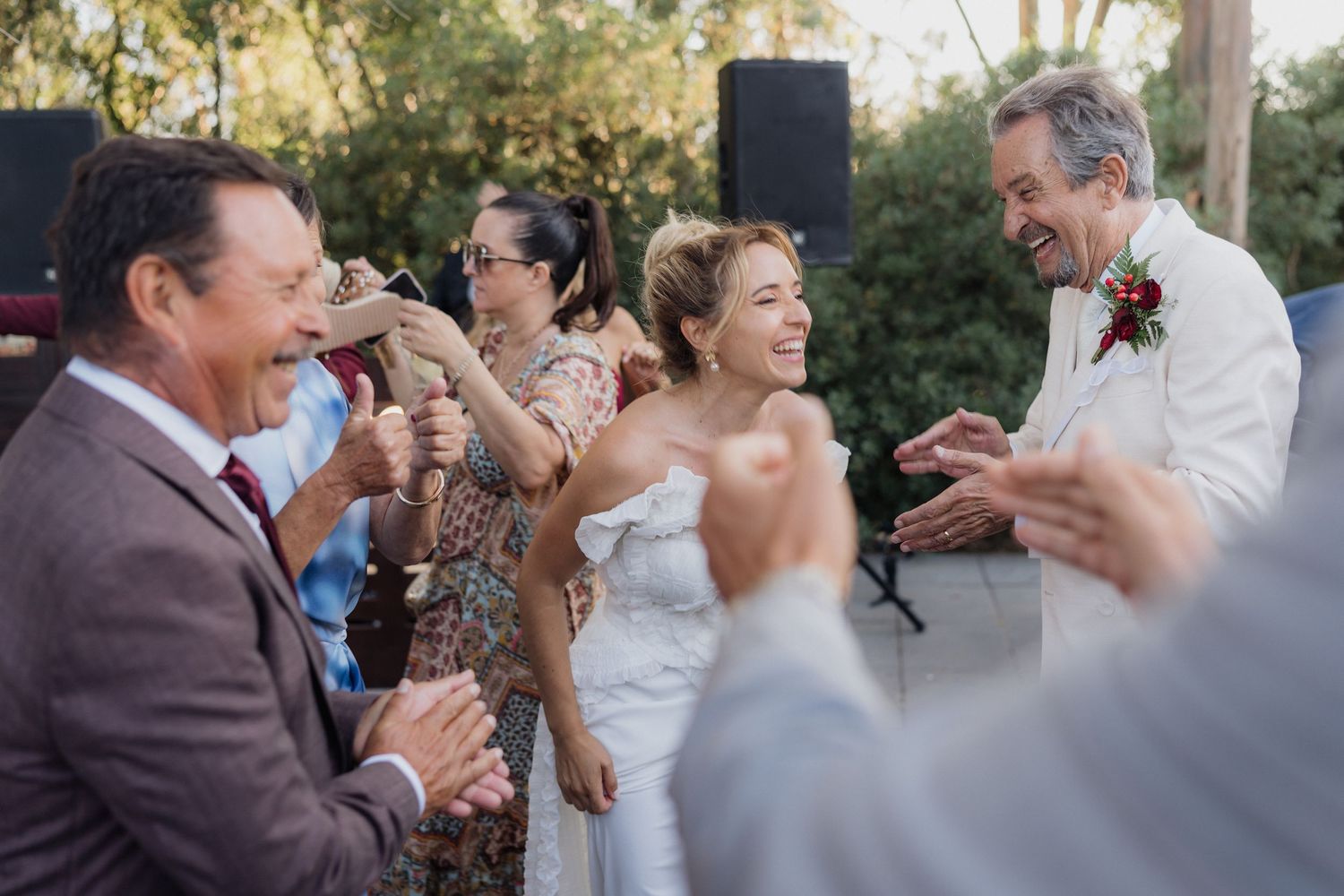 Wedding party members dance and celebrate at an outdoor venue.