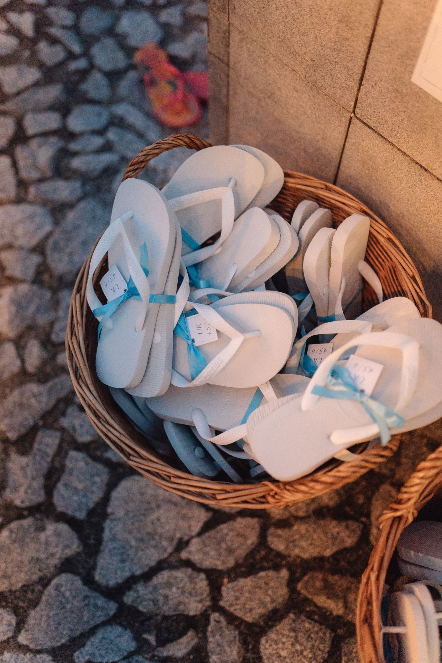 White flip flops arranged in a woven basket for wedding guests.