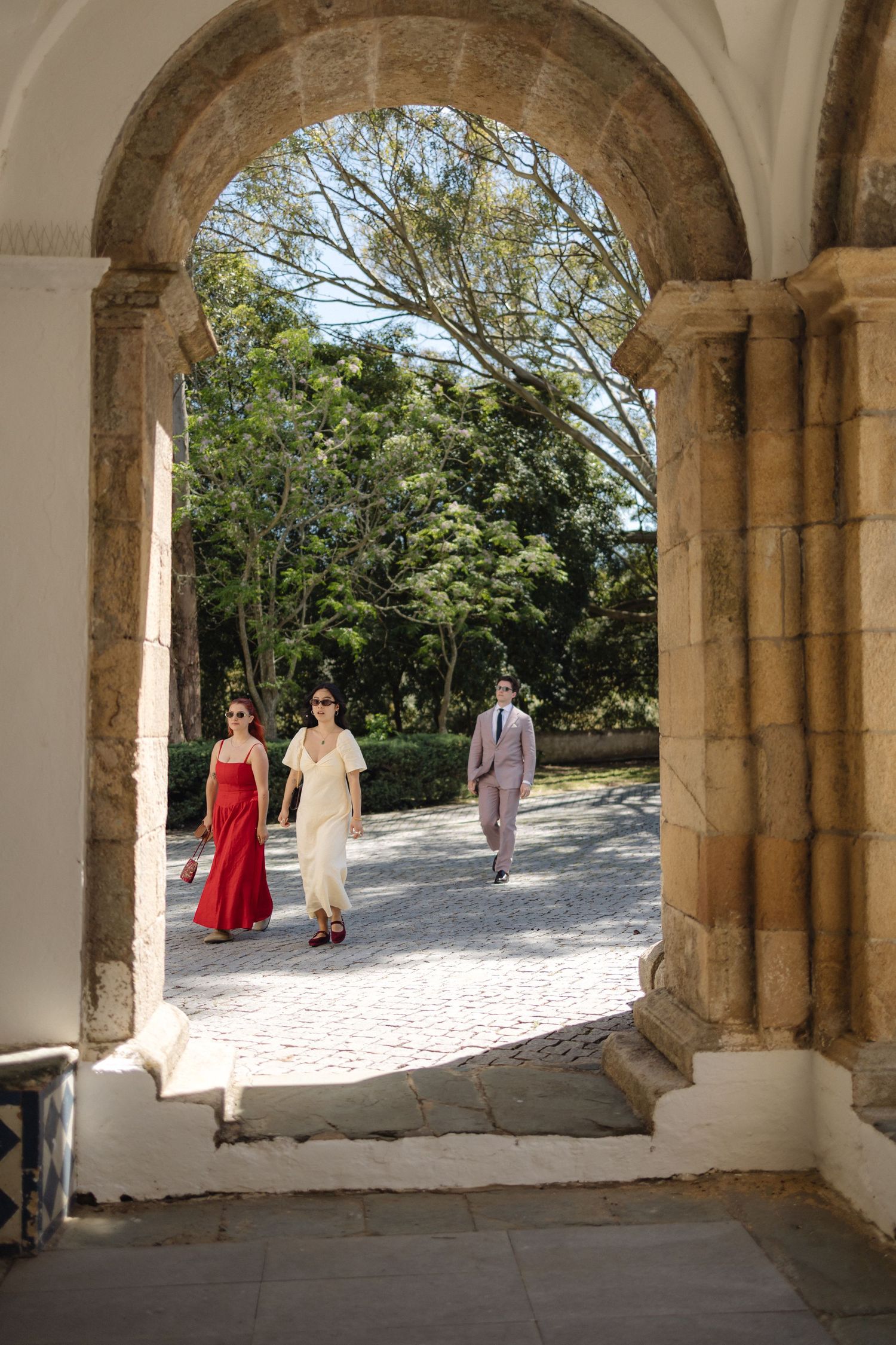 Stone archway corridor overlooking sunny courtyard with guests in formal attire.