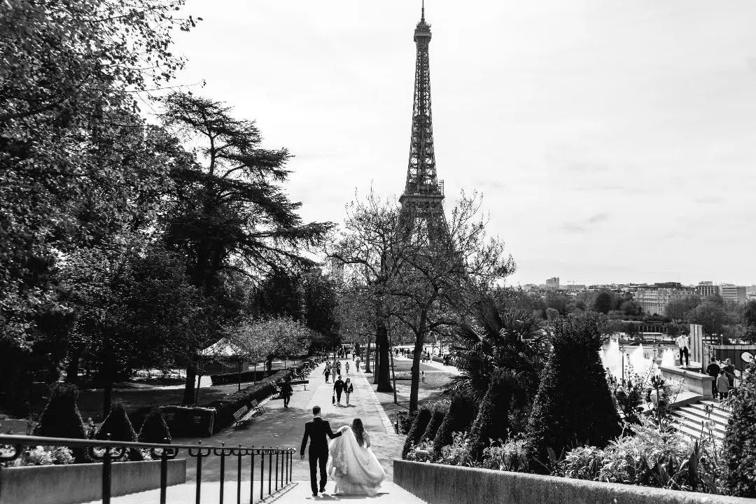 Black and white photo of a bride and groom walking near the Eiffel Tower in Paris, France.