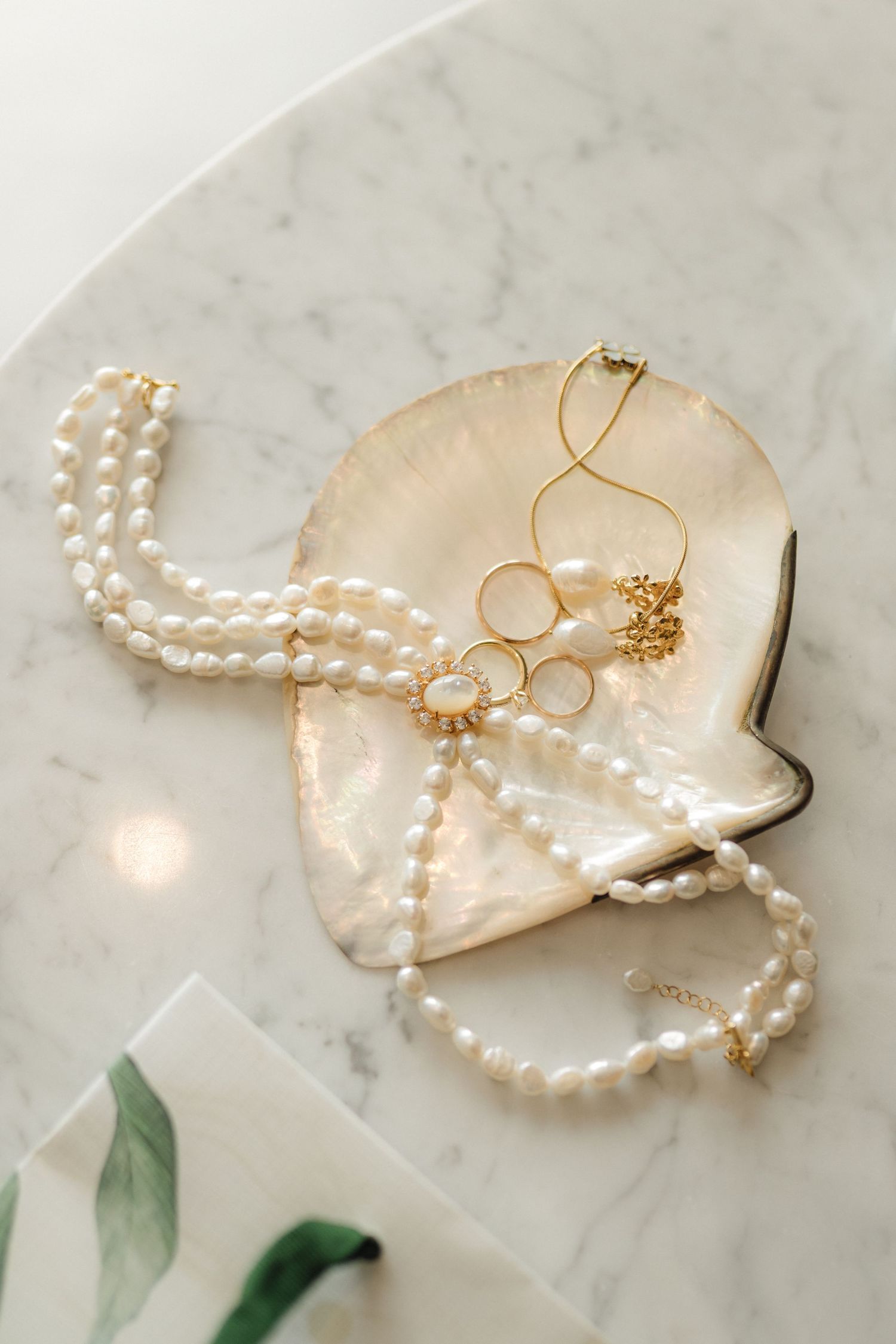 Delicate pearl necklace and gold jewelry arranged on marble surface with soft lighting.