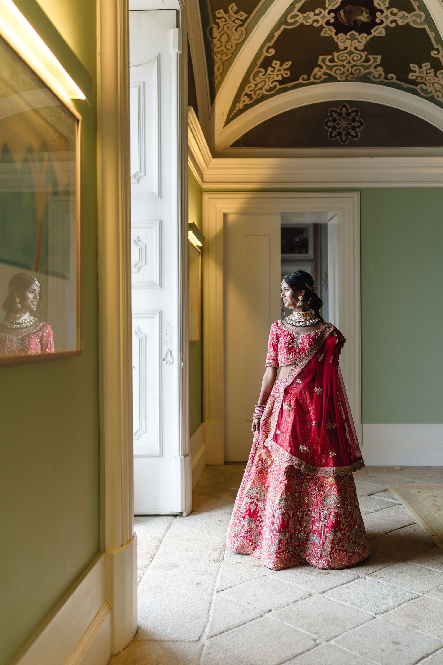 A red and gold embroidered lehenga photographed in an elegant room with arched ceilings and green walls.
