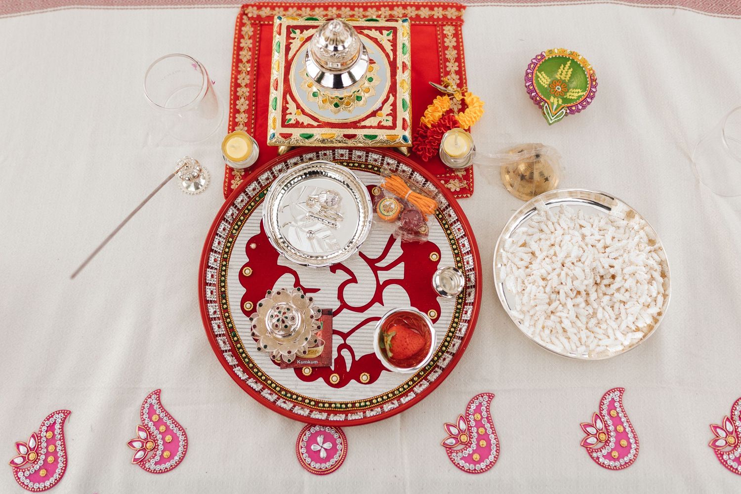 Traditional Indian wedding decorations with red and gold accents arranged on a white tablecloth.