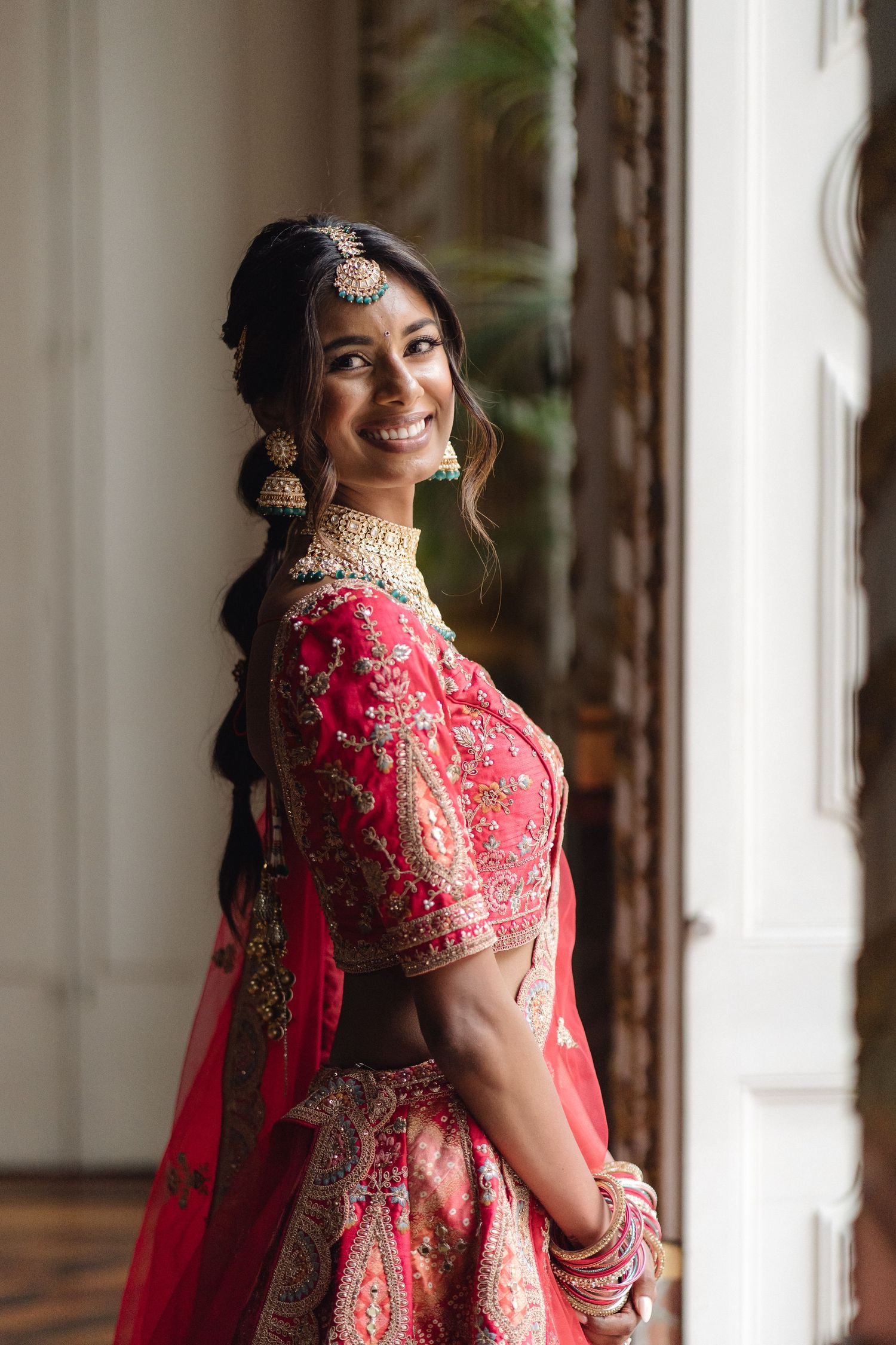 Bridal portrait in red and gold embroidered lehenga with traditional jewelry.