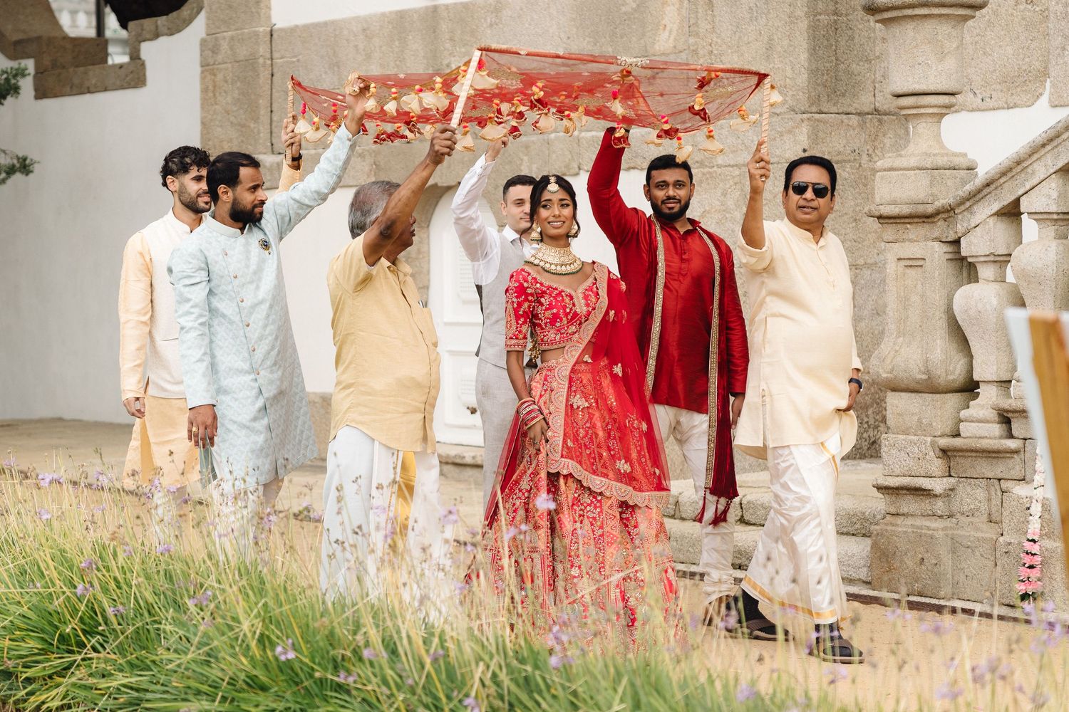 Wedding party members in white and red traditional Indian attire gathered outdoors.