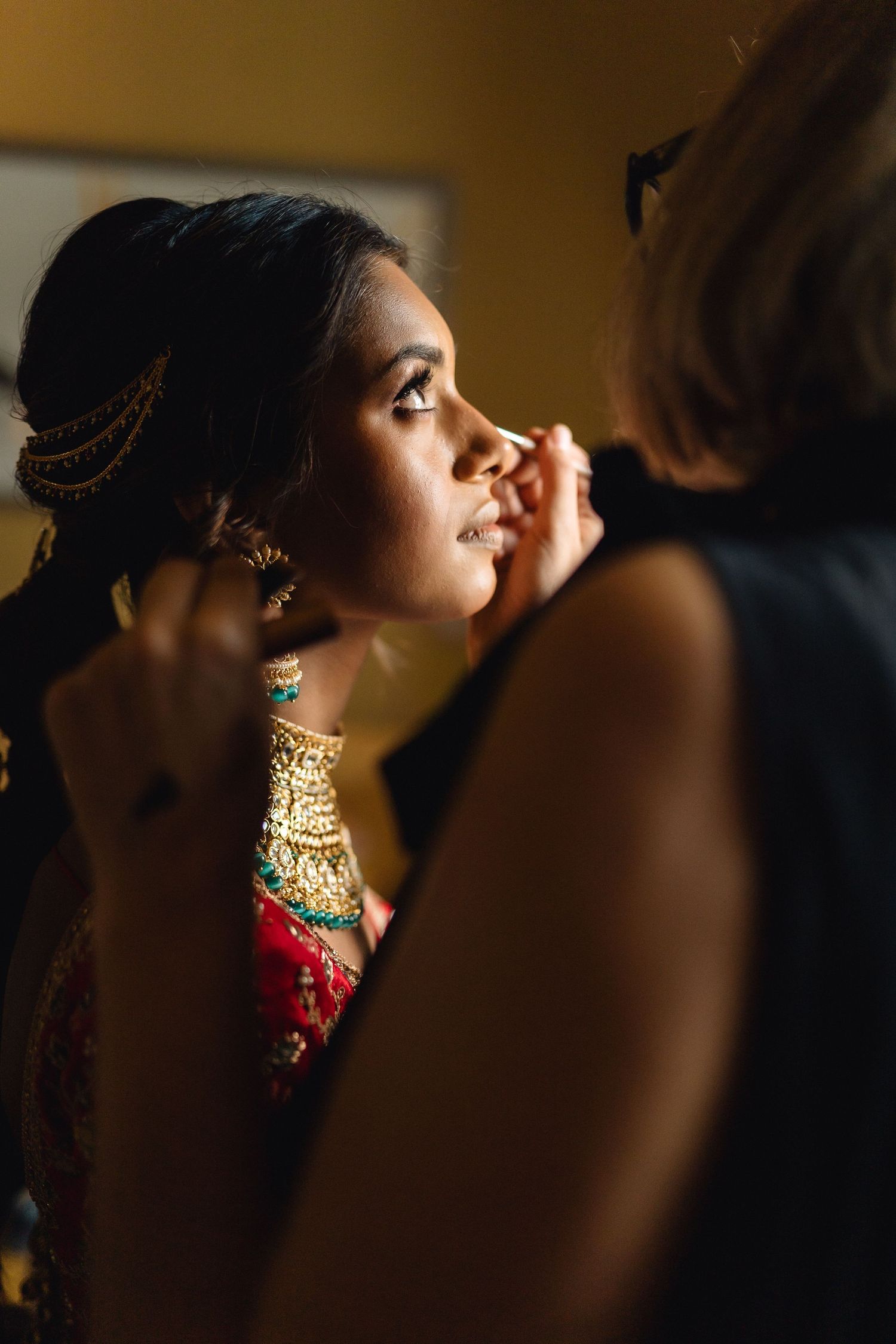 Close-up profile view of traditional Indian bridal jewelry and makeup in warm lighting.