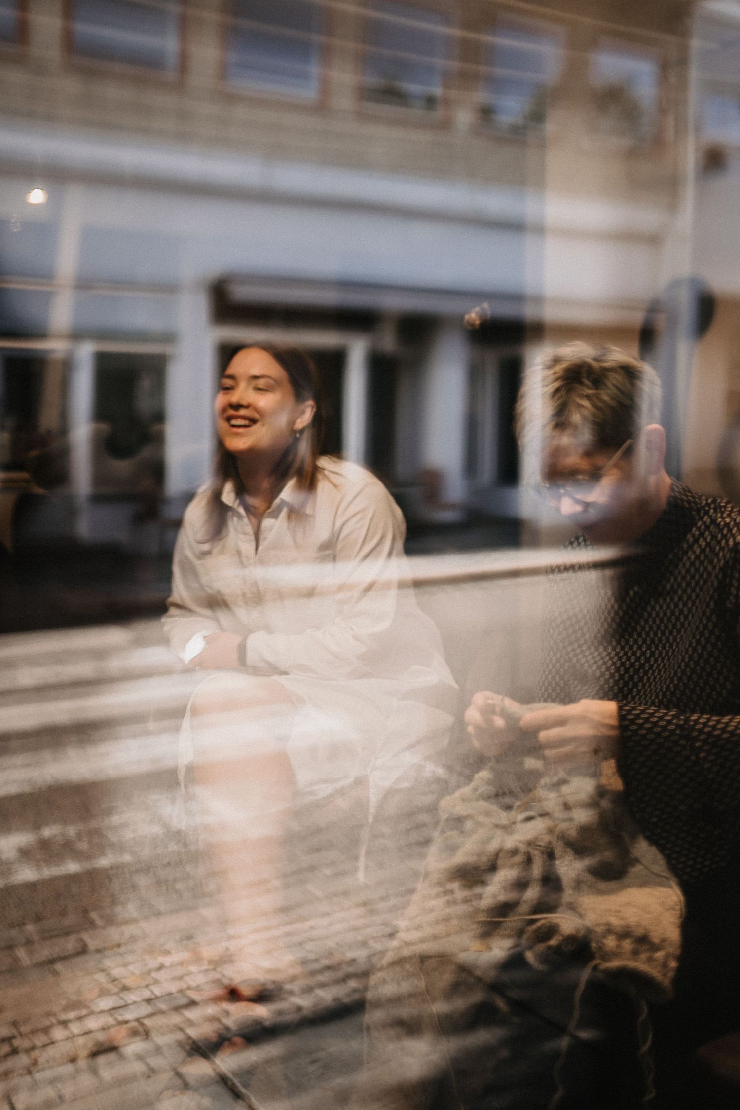 Artistic reflection through window glass showing blurred figures in natural light.