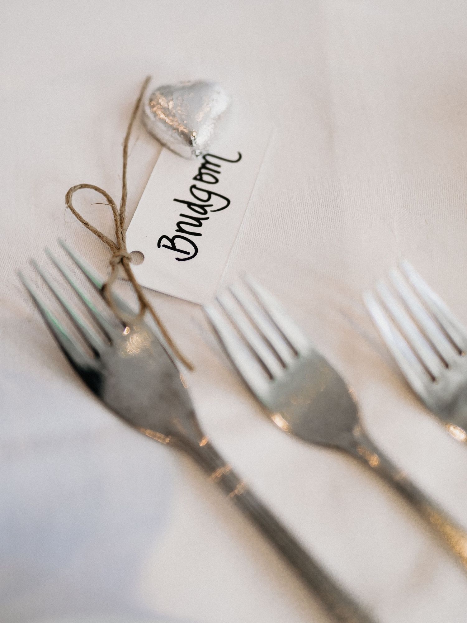 Elegant place settings with vintage silver forks tied with twine and name cards on white linens.