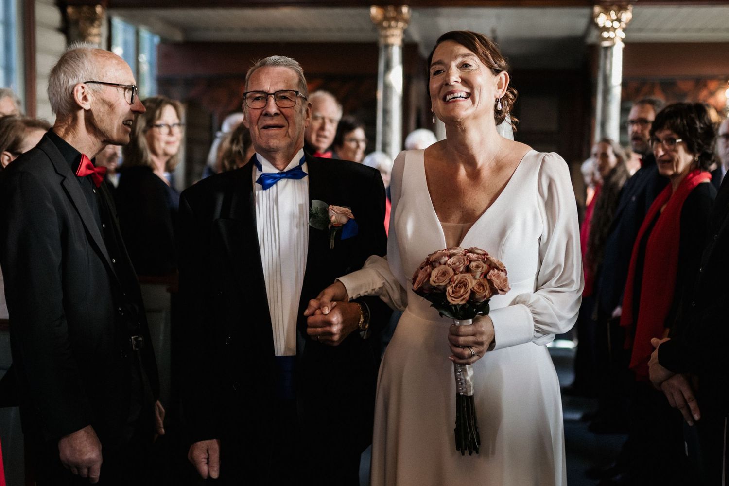 Wedding ceremony guests gathered in formal attire at an indoor venue.