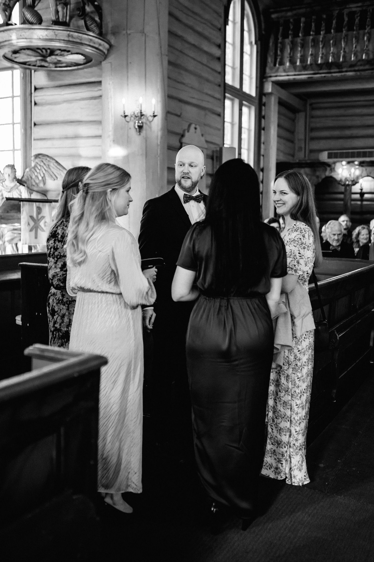 Wedding guests mingling inside a rustic church interior with wooden beams and chandeliers.