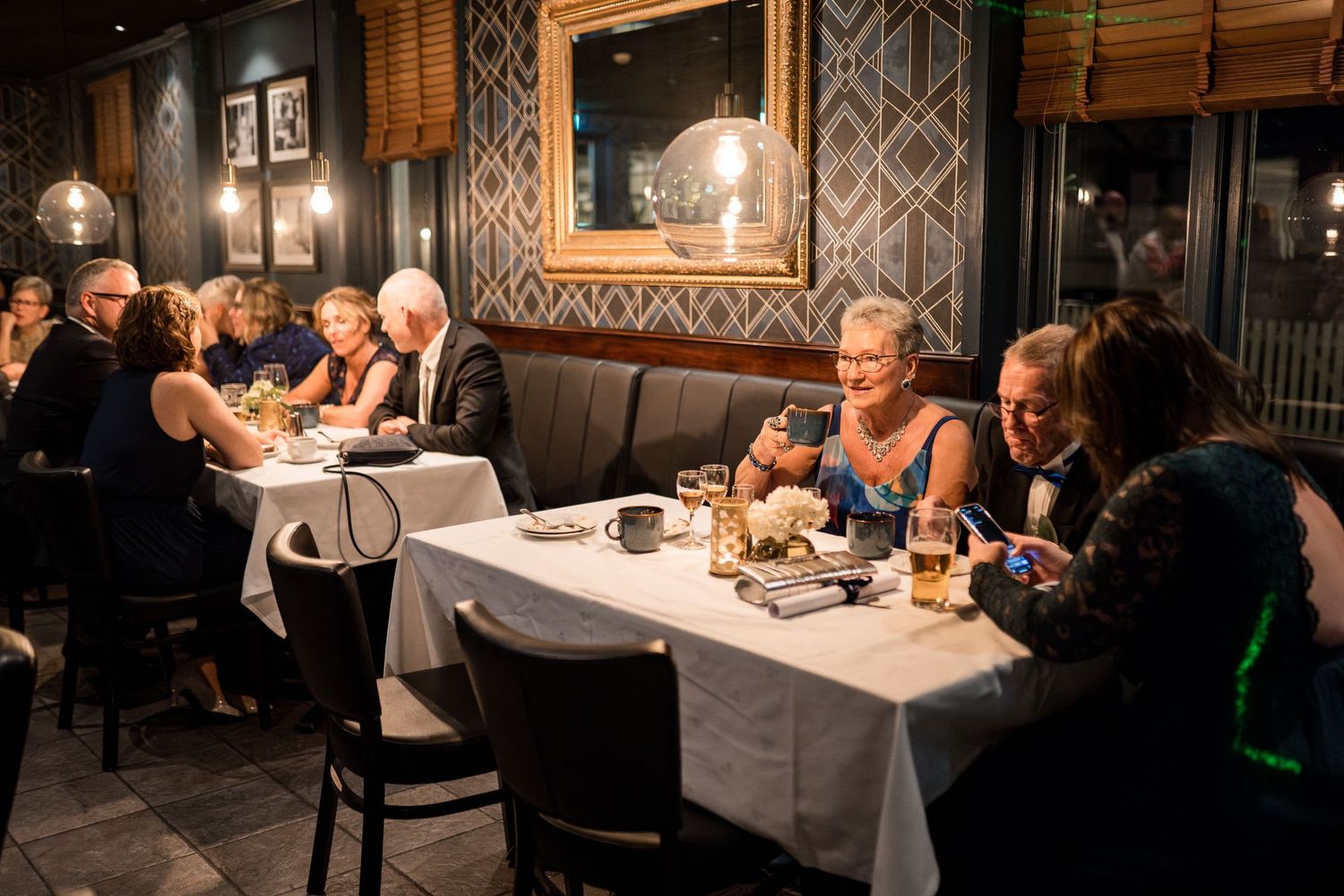 Vintage-style restaurant interior with ornate wallpaper and mirrors showing diners at candlelit tables.