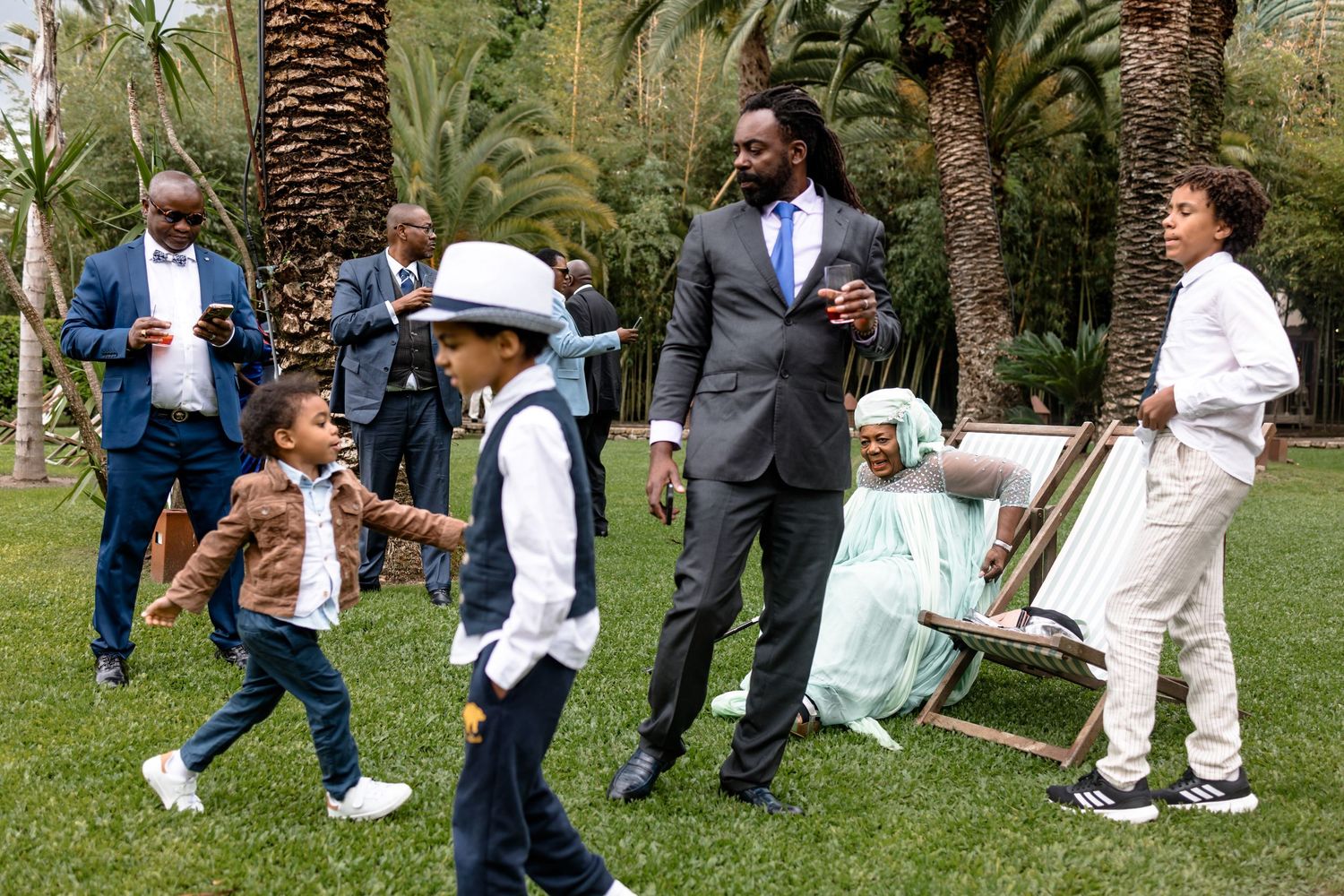 Wedding guests mingle and socialize on a lush palm-tree lined garden path.