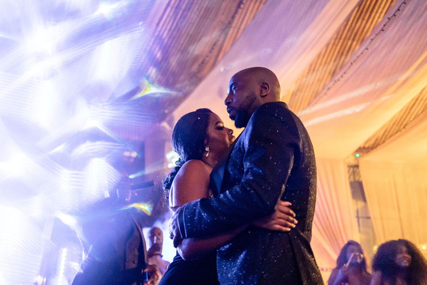 Couples dancing under purple and blue lighting effects at a wedding reception.