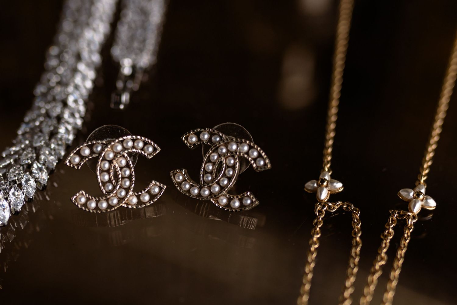 Elegant jewelry display featuring sparkling crystal Chanel logo earrings and necklaces on dark background.