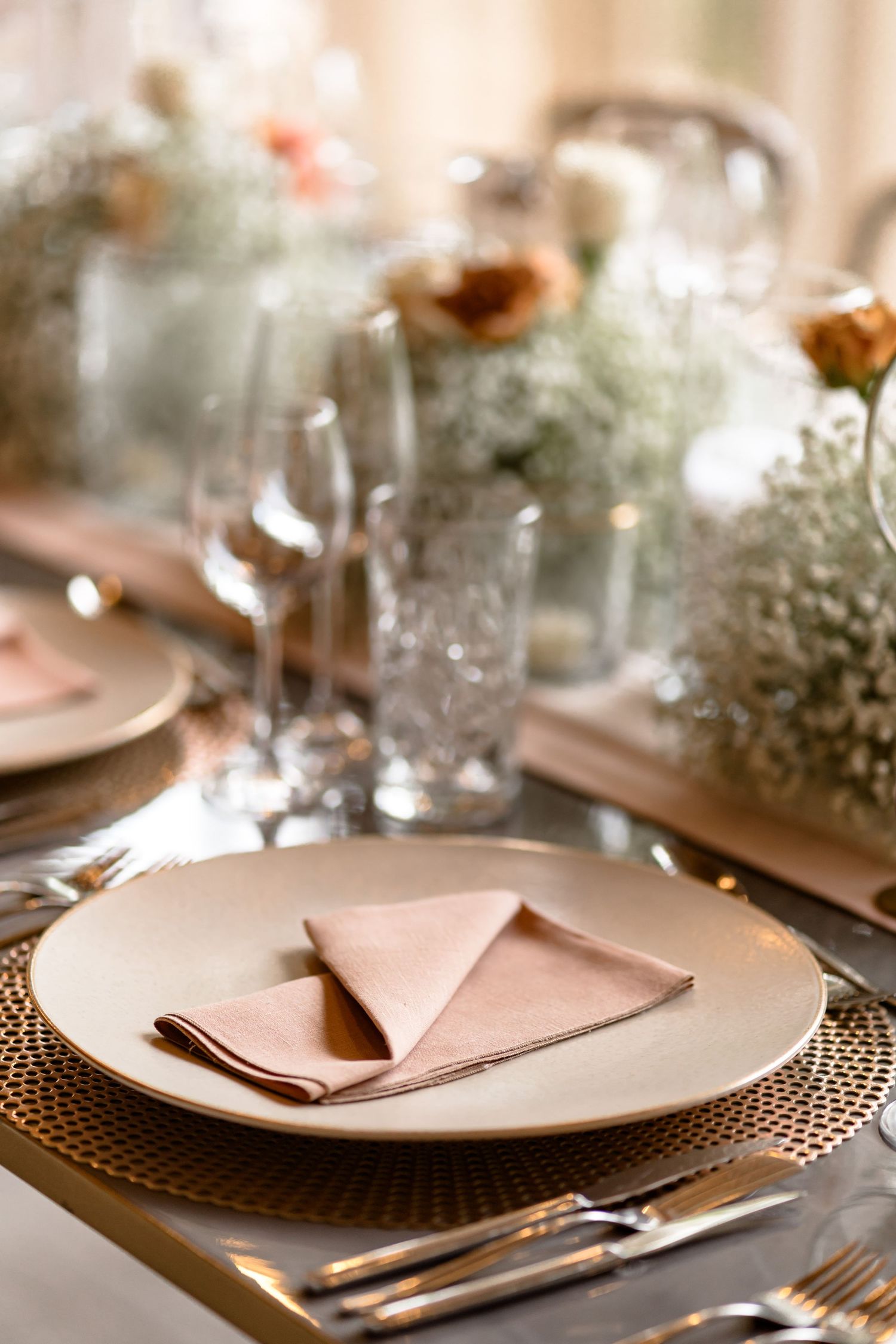 Elegant place settings with blush napkins and gold charger plates at wedding reception.