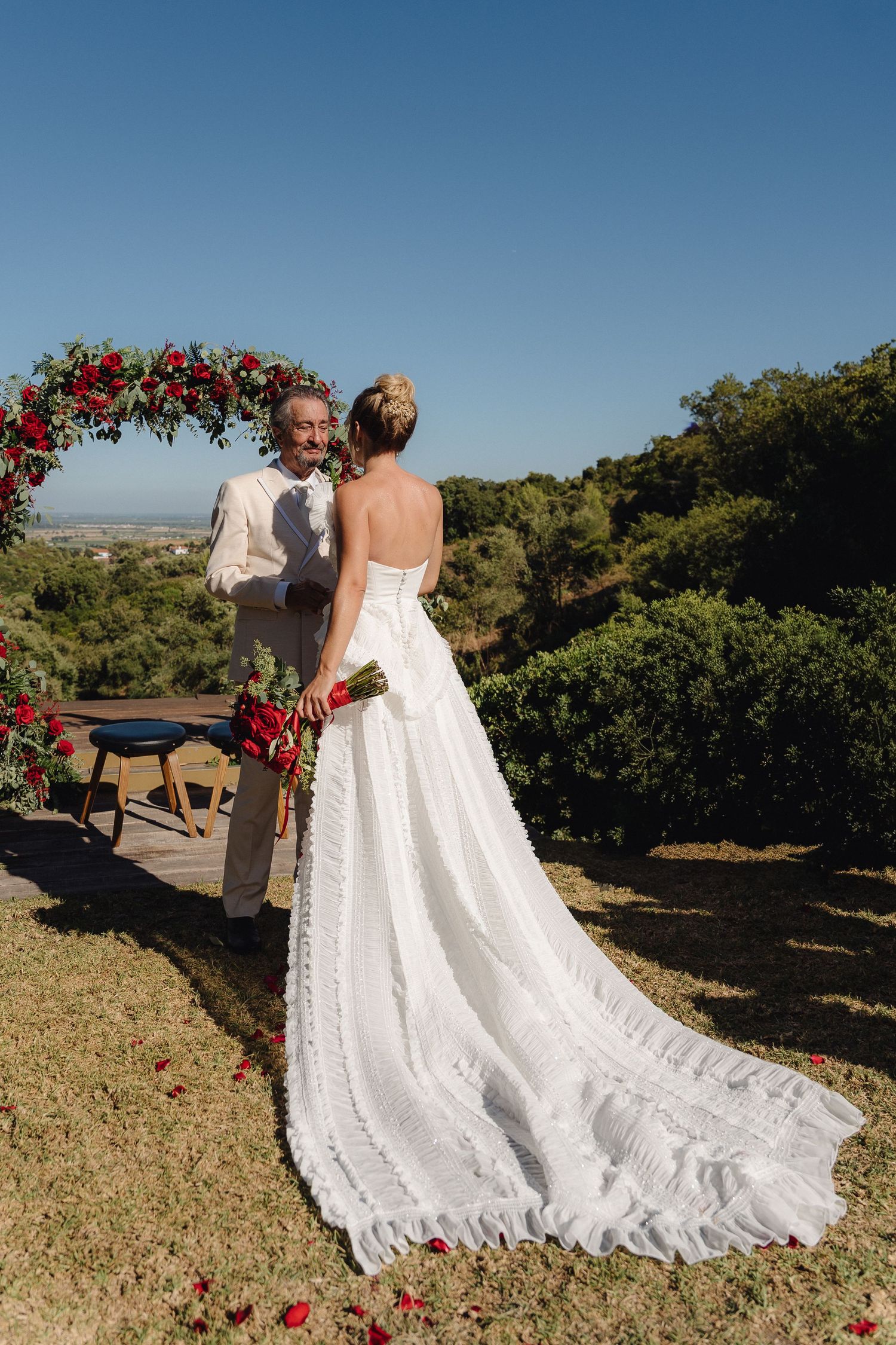 White wedding dress with long train photographed against blue sky and natural landscape.