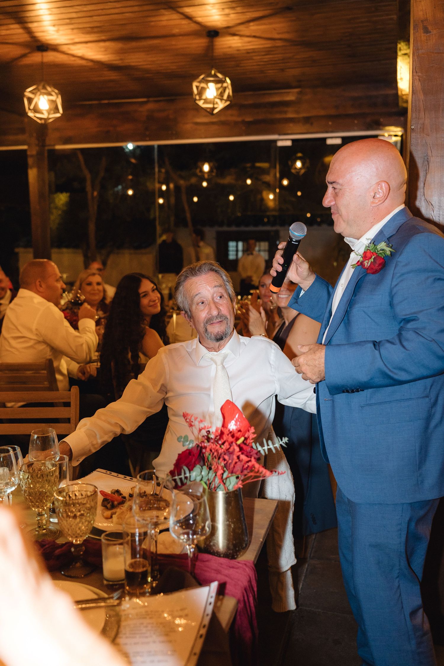 Wedding celebration in a wooden venue with guests seated at decorated tables and ambient lighting.