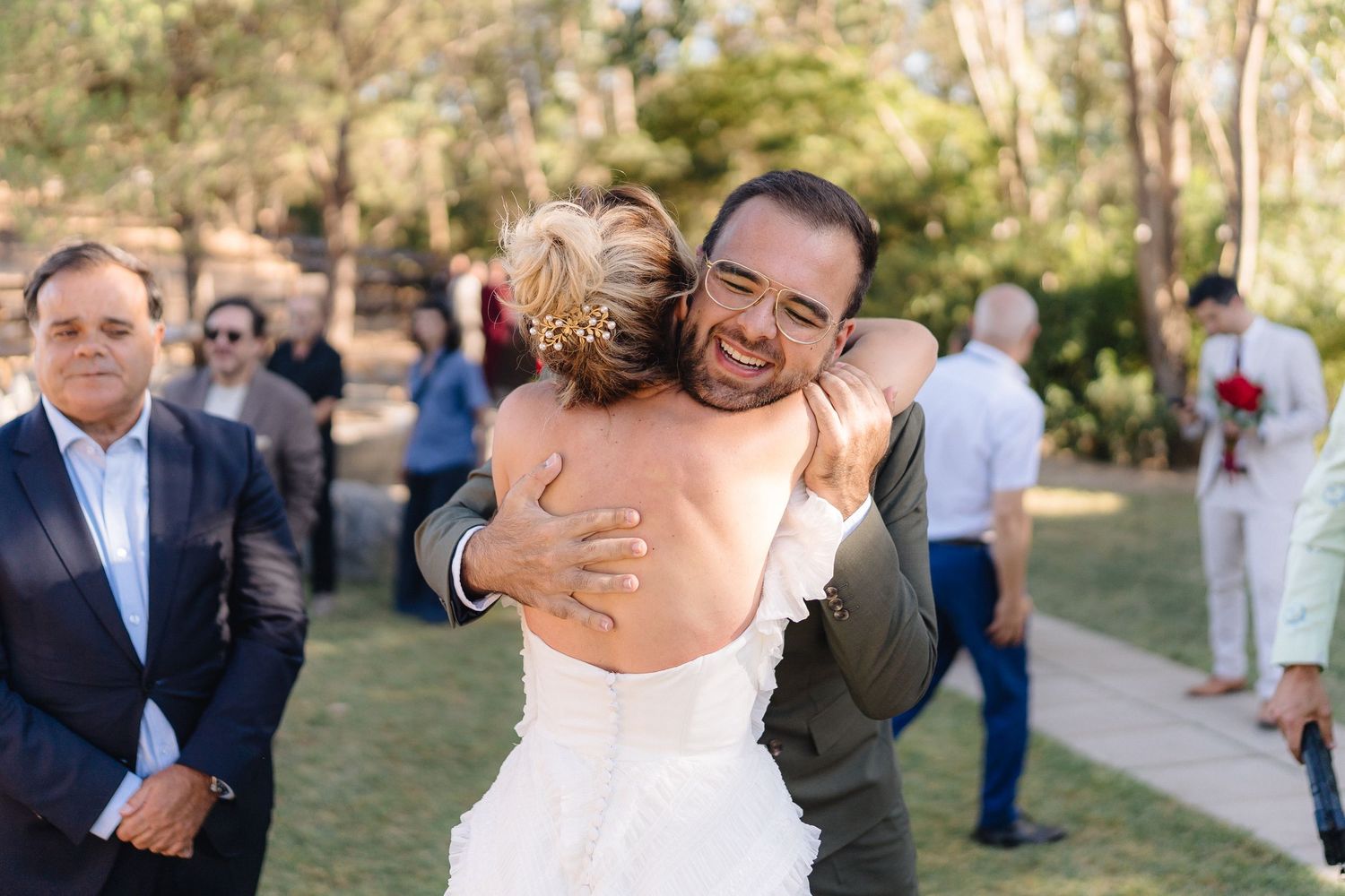 Wedding party members share warm hugs during an outdoor celebration.