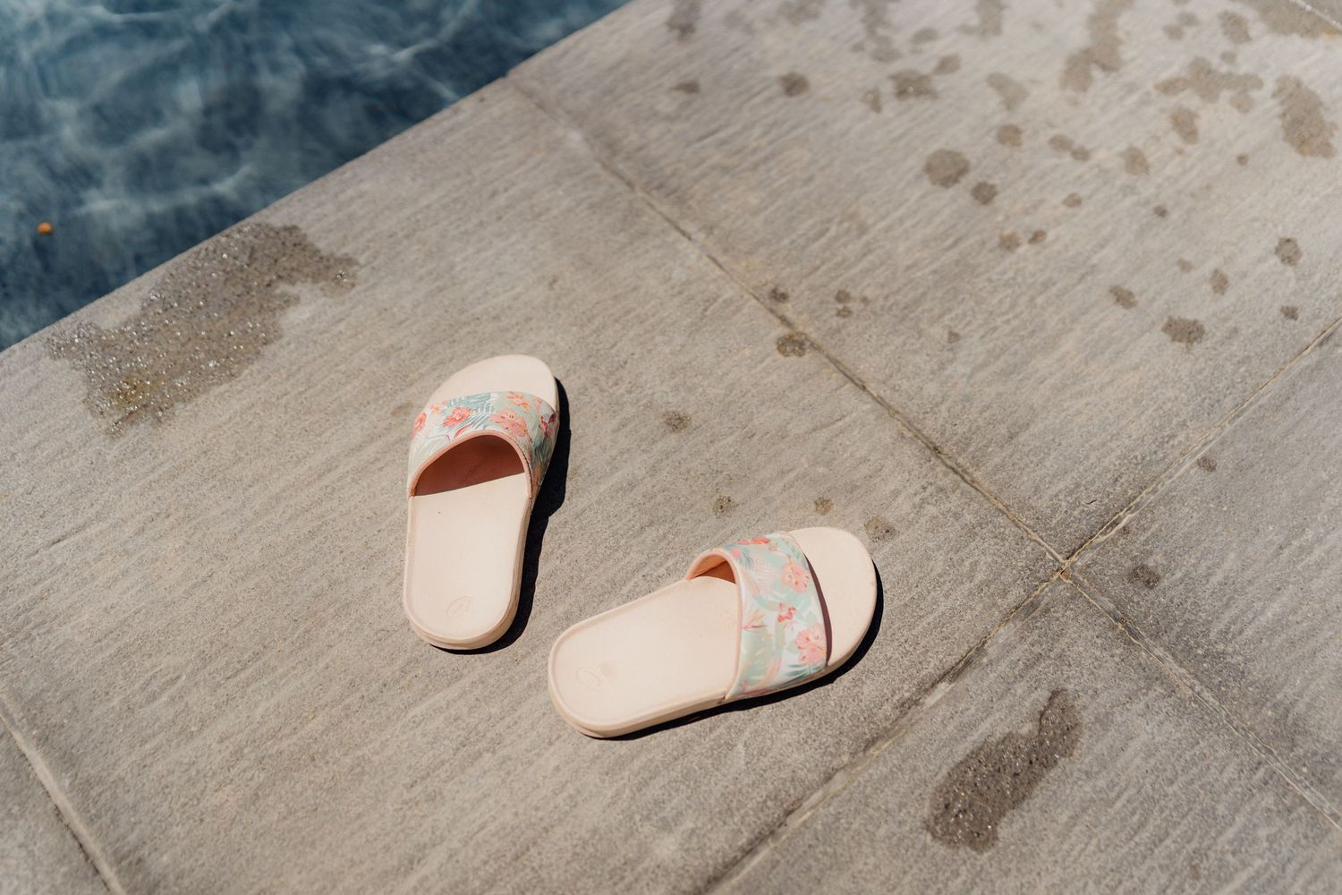 White sandals left on a concrete surface near water.