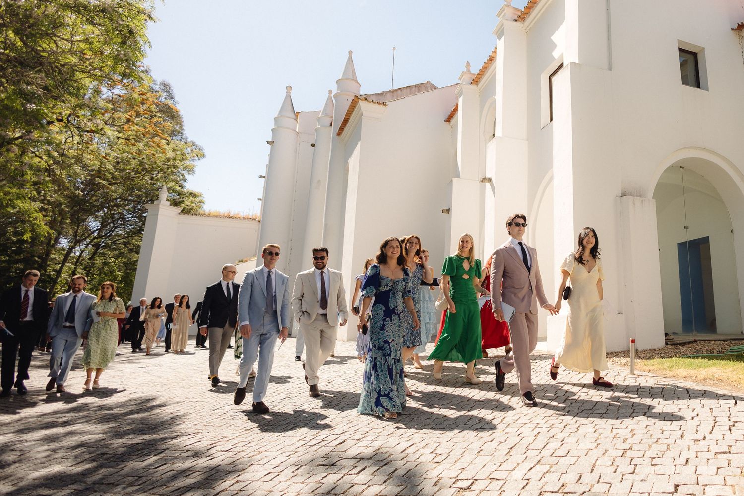 White stone church exterior with arched doorways and wedding guests gathered outside.