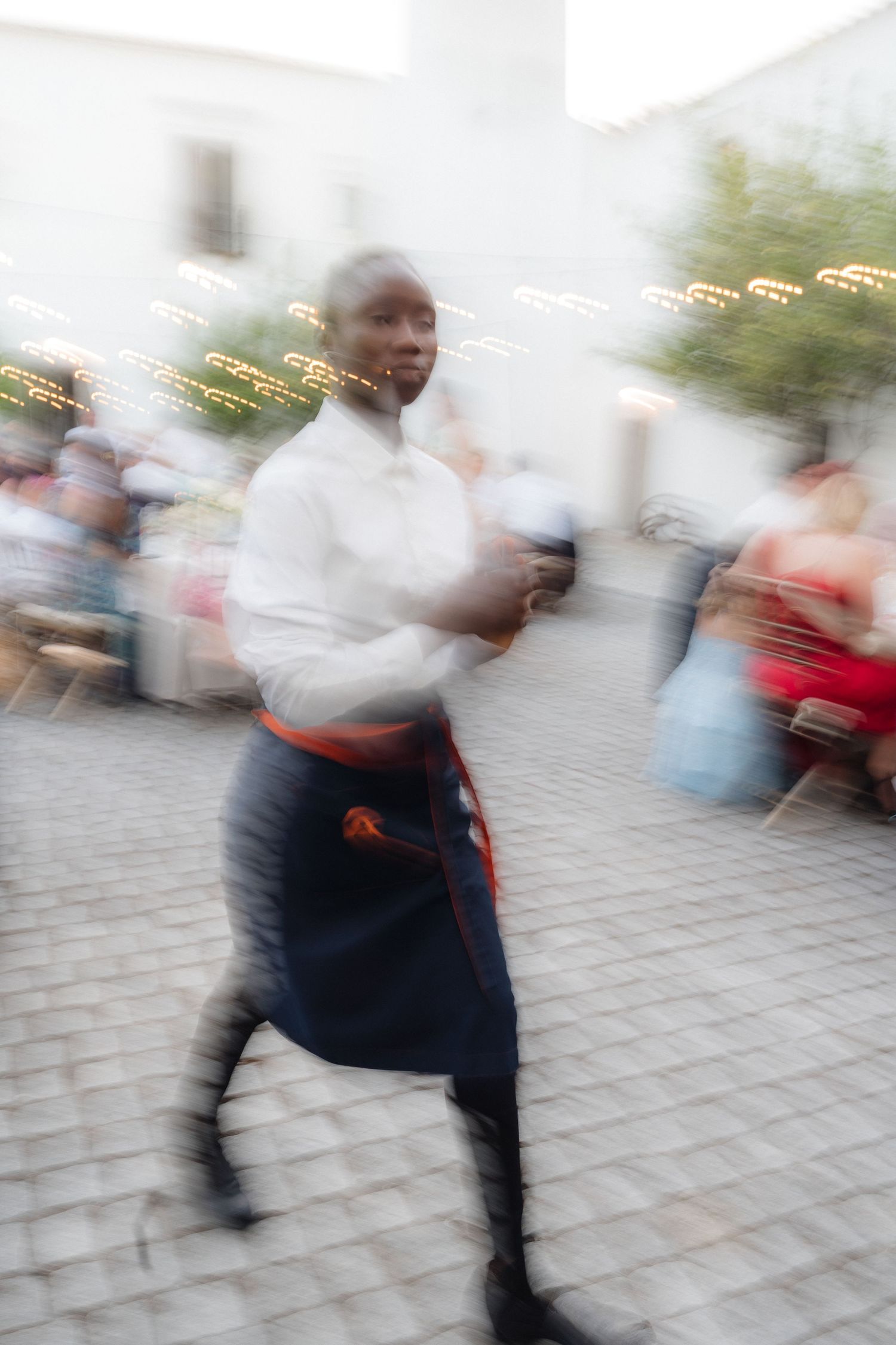 Motion-blurred image of people walking on cobblestone pavement during an evening event.