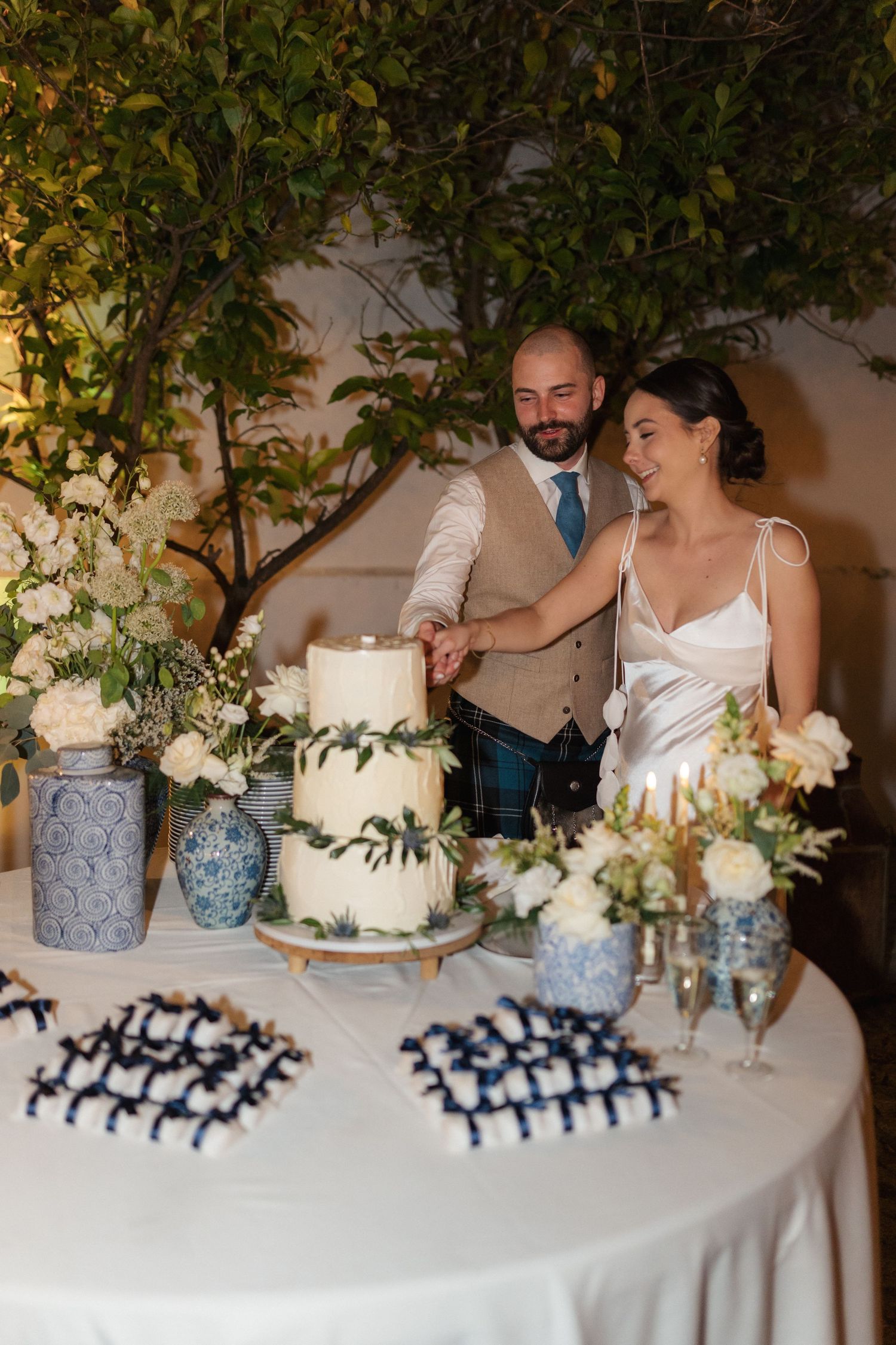 Wedding cake cutting moment with elegant floral decorations and blue ceramic vases.