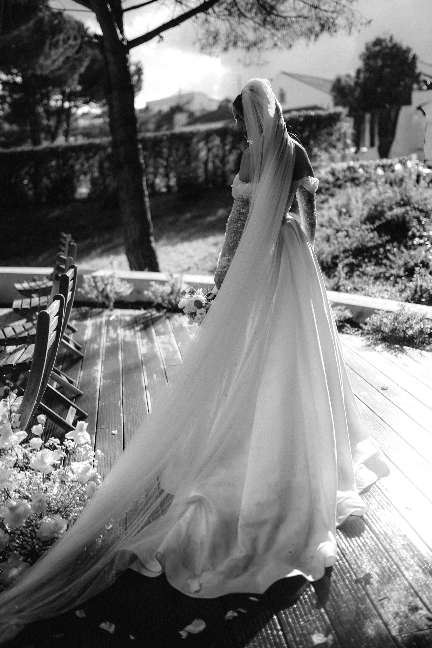 Artistic black and white photo of a flowing wedding dress skirt on a wooden deck in natural light.