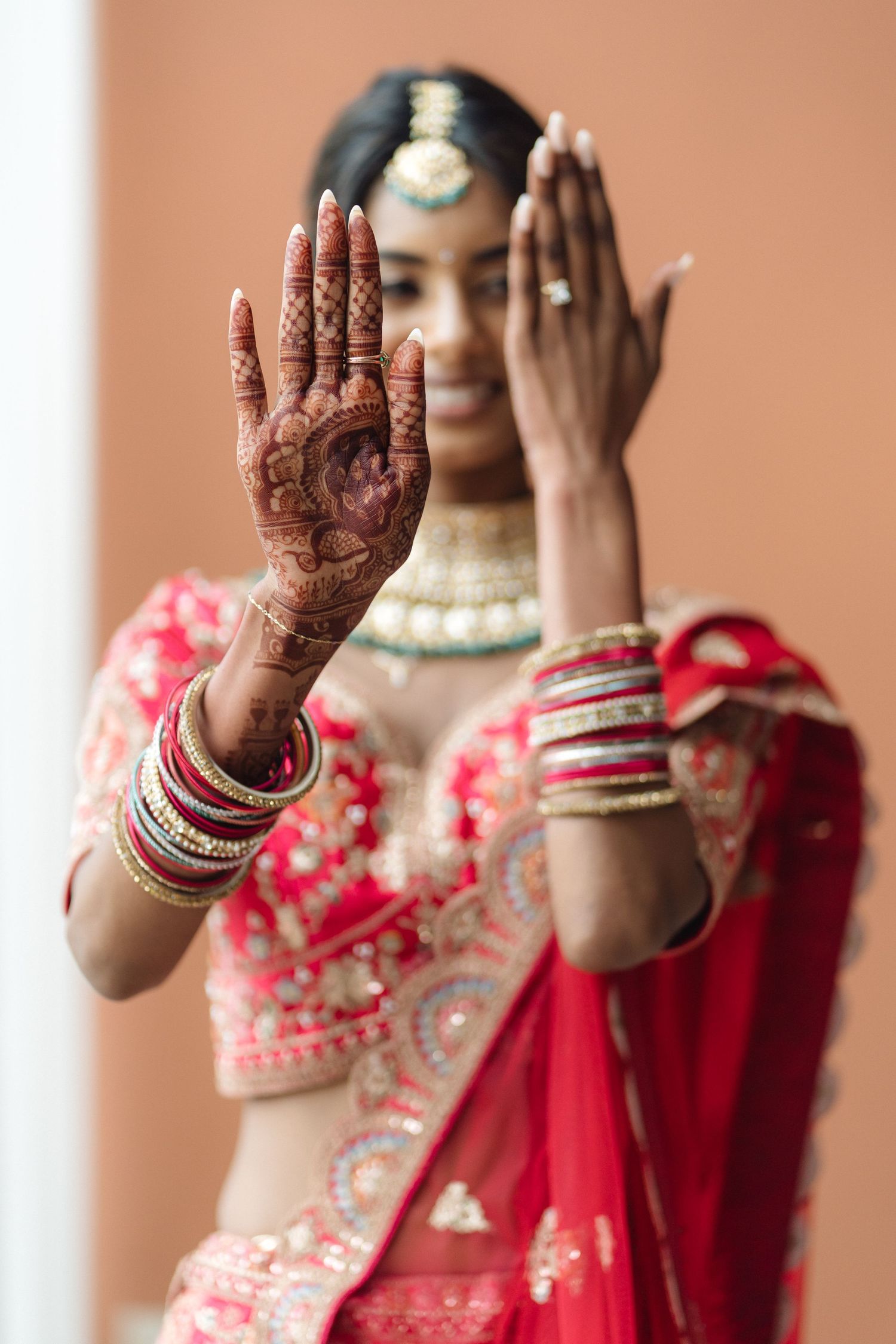 Close-up of hands with intricate henna designs and red bridal bangles.