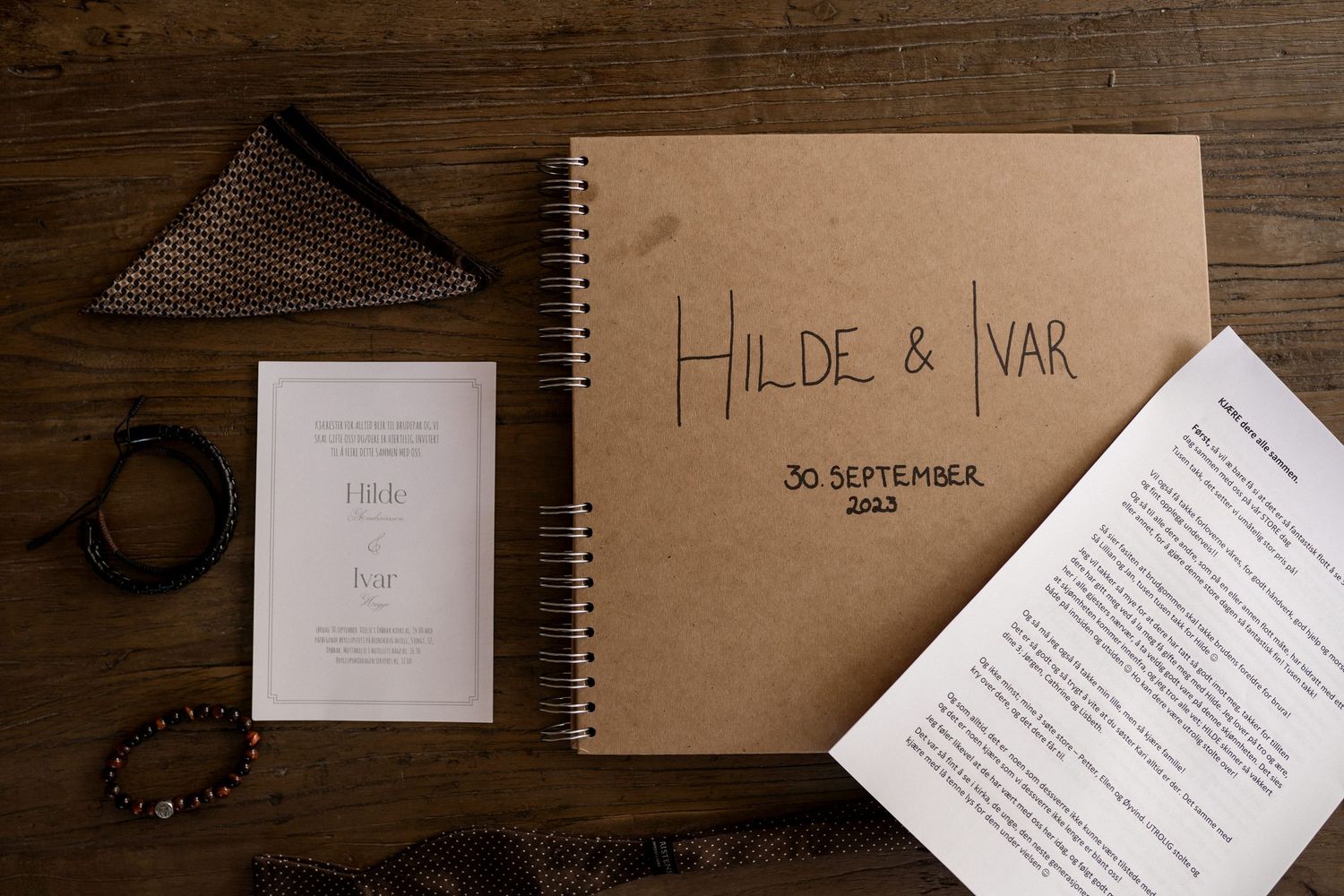 Wedding invitation suite with brown kraft paper envelopes and white cards laid out on a dark wooden surface.