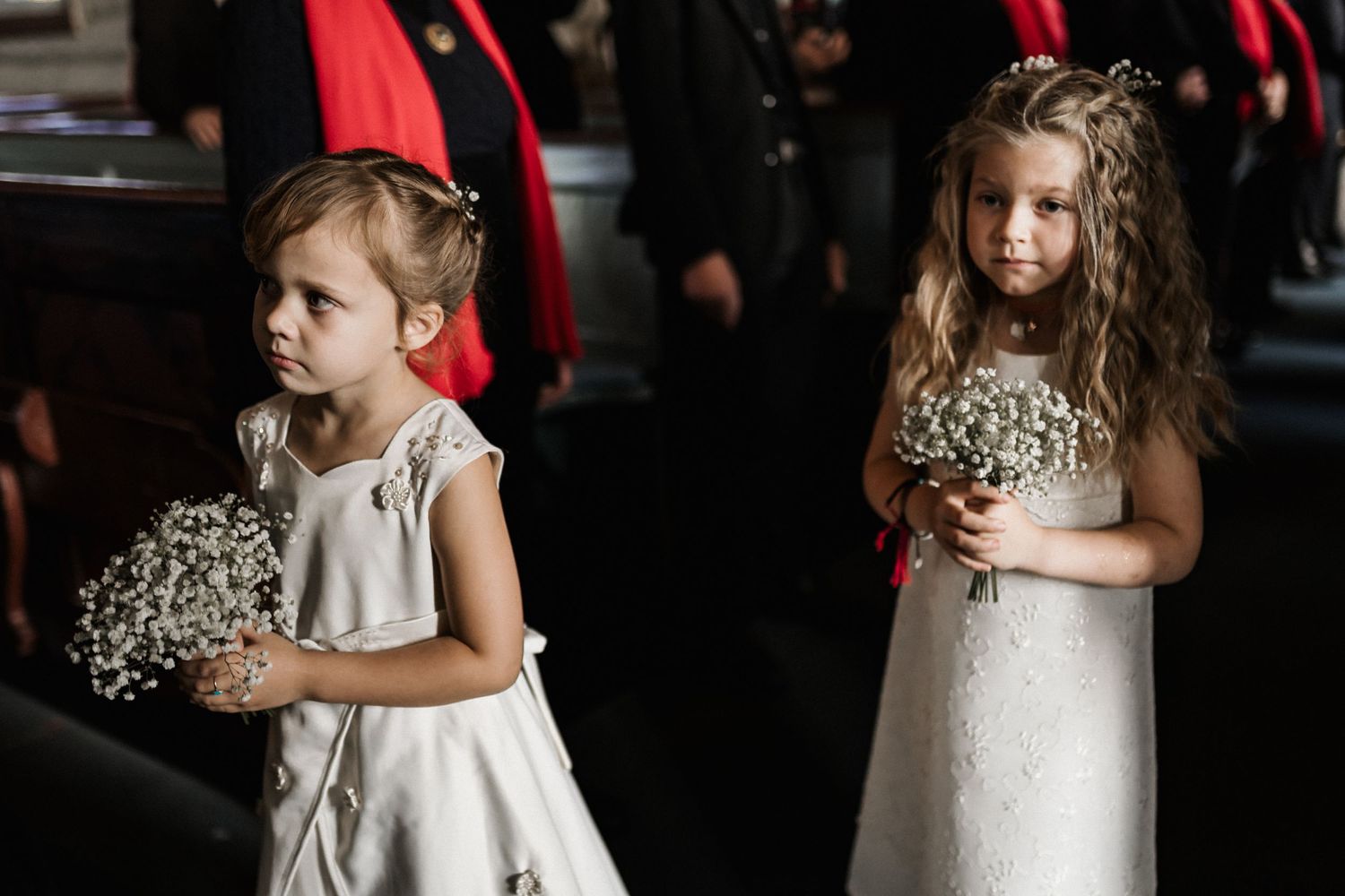 Young flower girls in white dresses holding bouquets at a wedding ceremony.