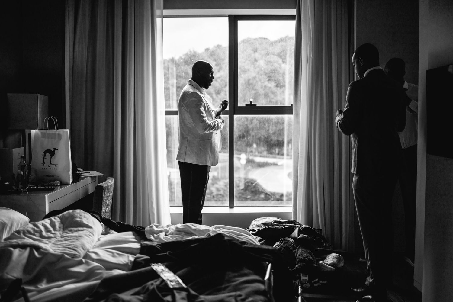Wedding party members getting ready in a hotel room with natural window lighting.