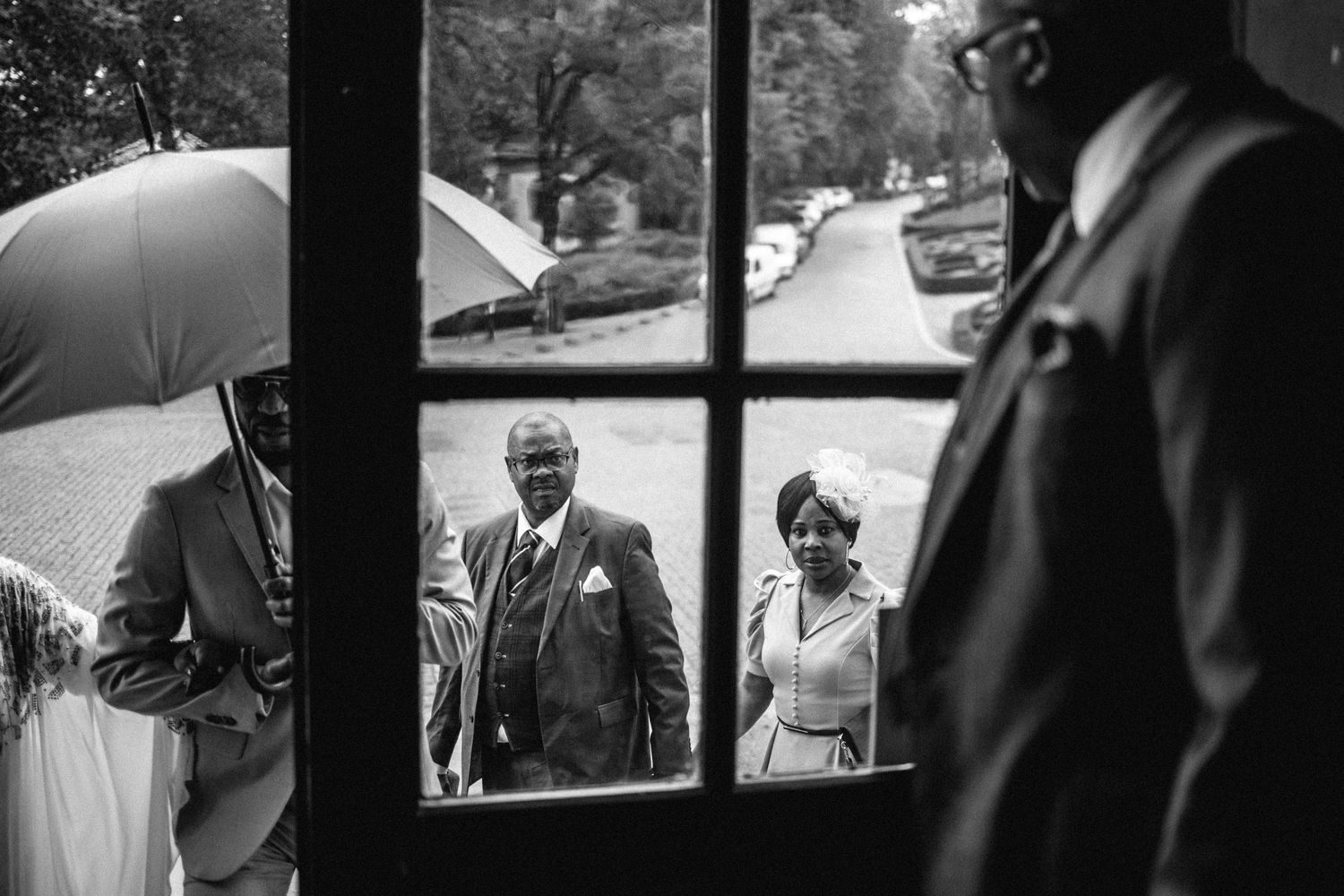 Documentary style black and white photography of wedding guests through window panes.