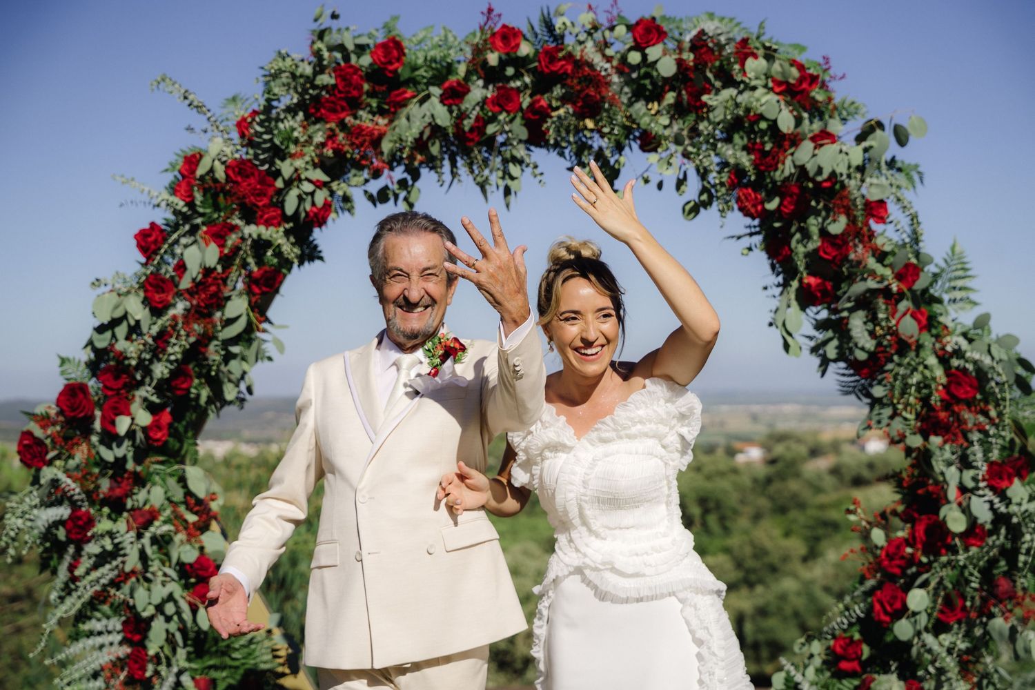 Wedding ceremony setup with red floral arch against blue sky backdrop.