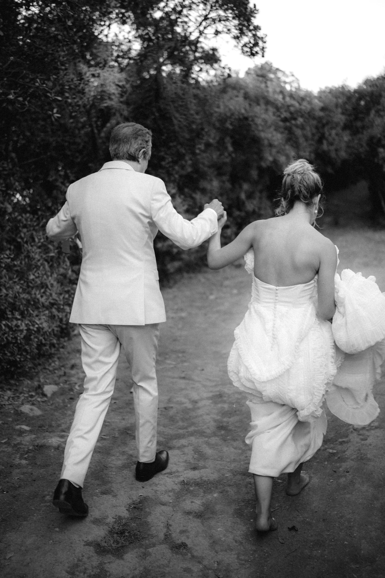 Black and white photo of couple running playfully through a garden path.